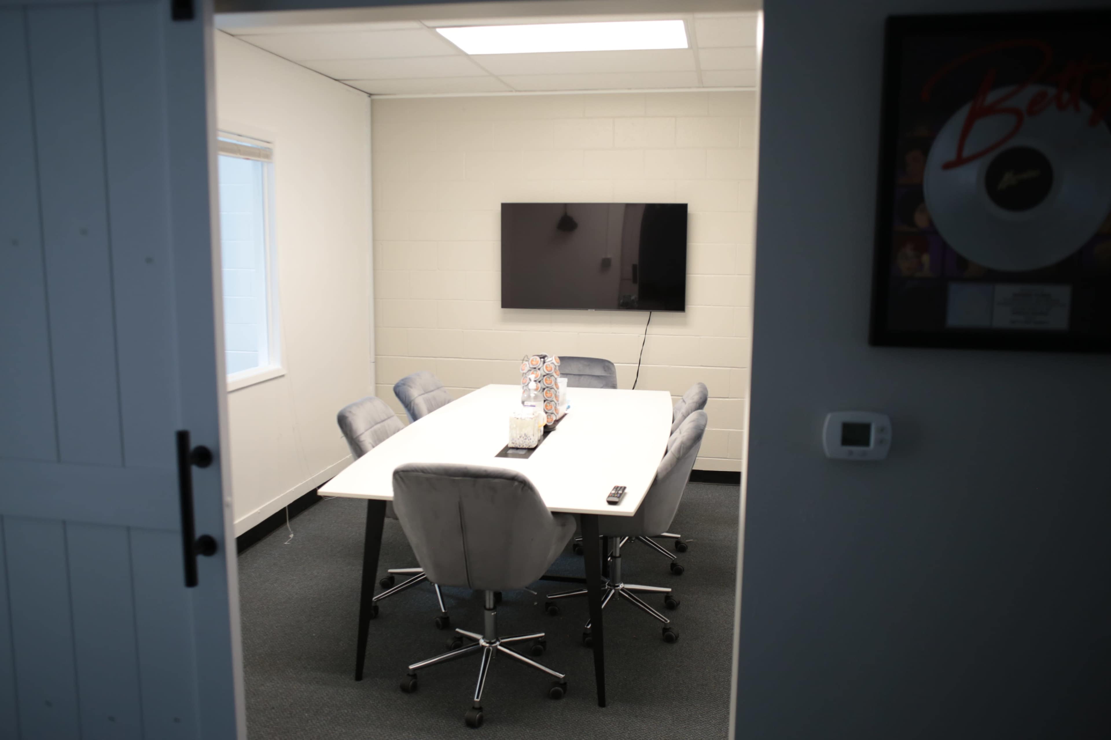 A modern conference room with a rectangular table surrounded by six plush chairs and a wall-mounted television.