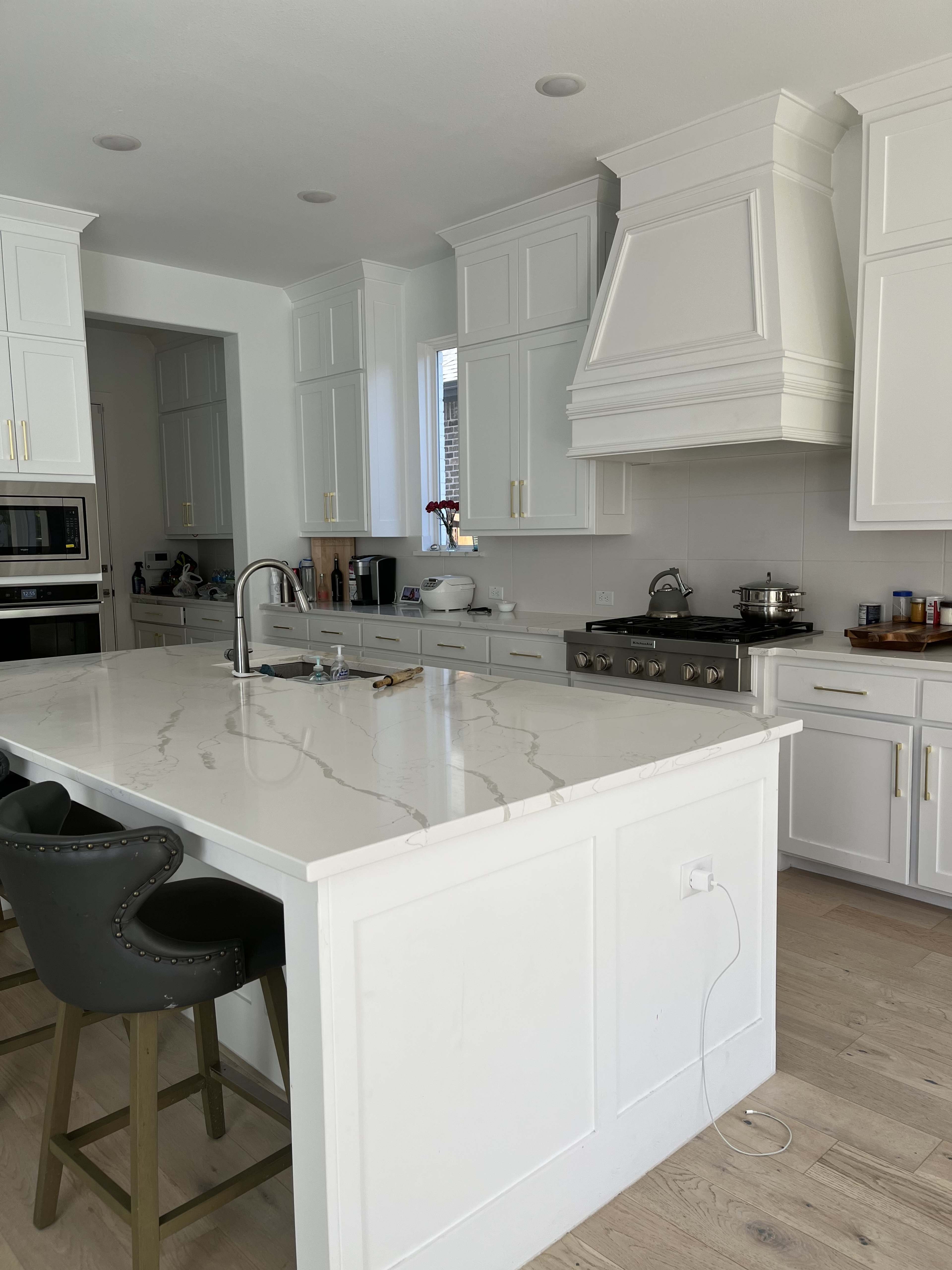 A modern kitchen features white cabinetry, a large island with a marble countertop, and stainless steel appliances.