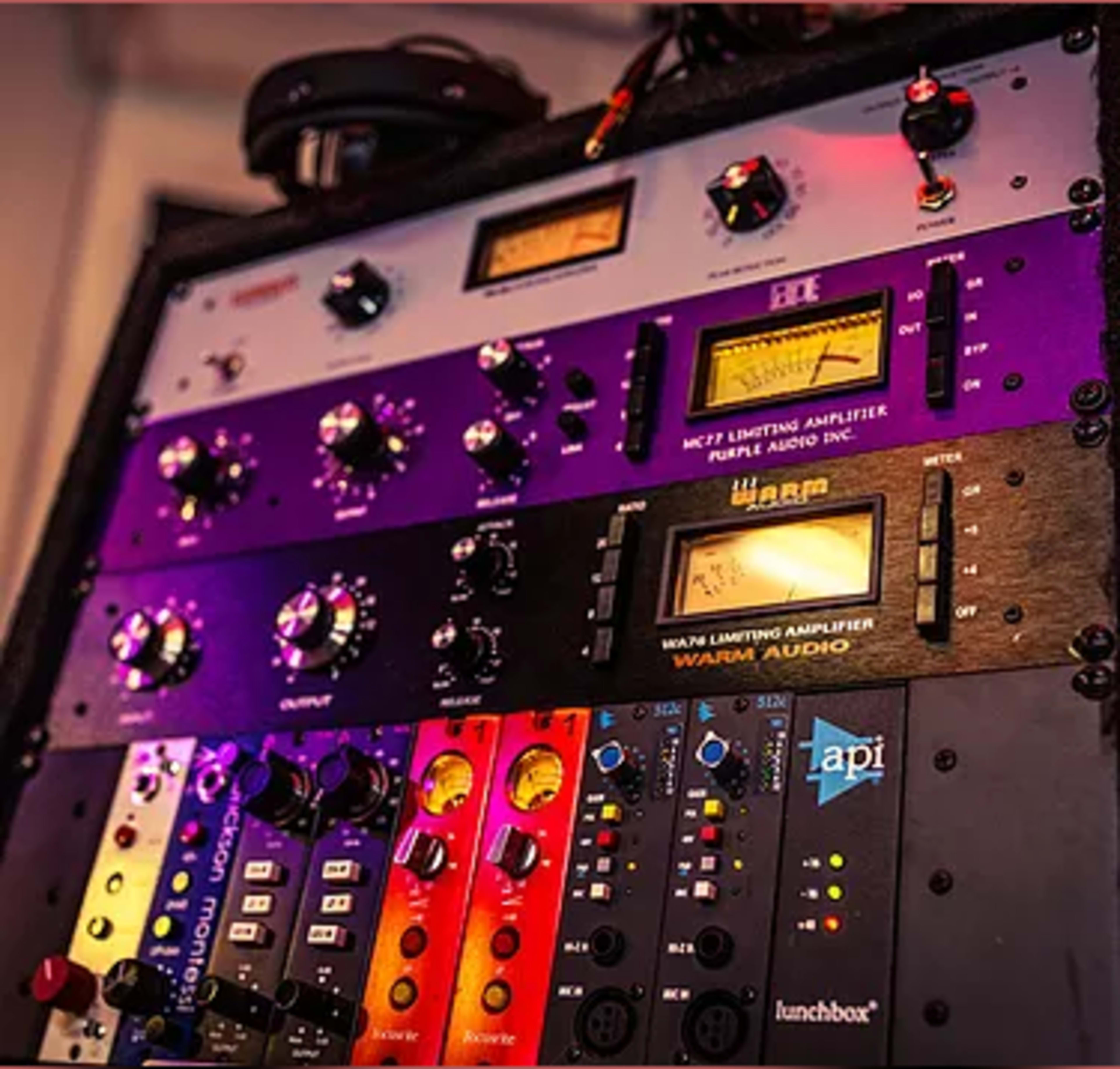 A rack of audio equipment featuring multiple limiting amplifiers and signal processors with illuminated meters and various control knobs.