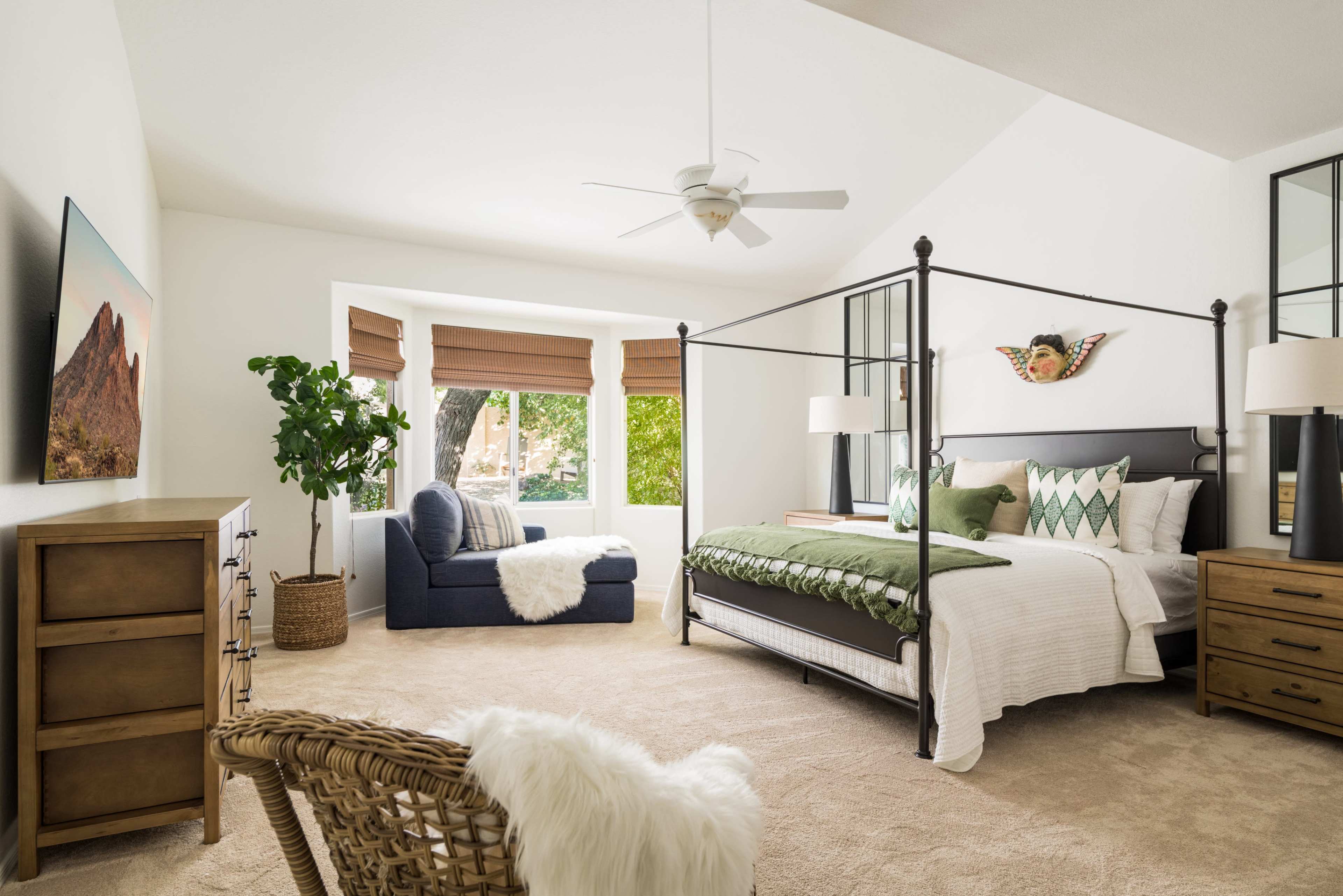 A spacious bedroom featuring a four-poster bed, a comfortable chair, and large windows with natural light filtering in.
