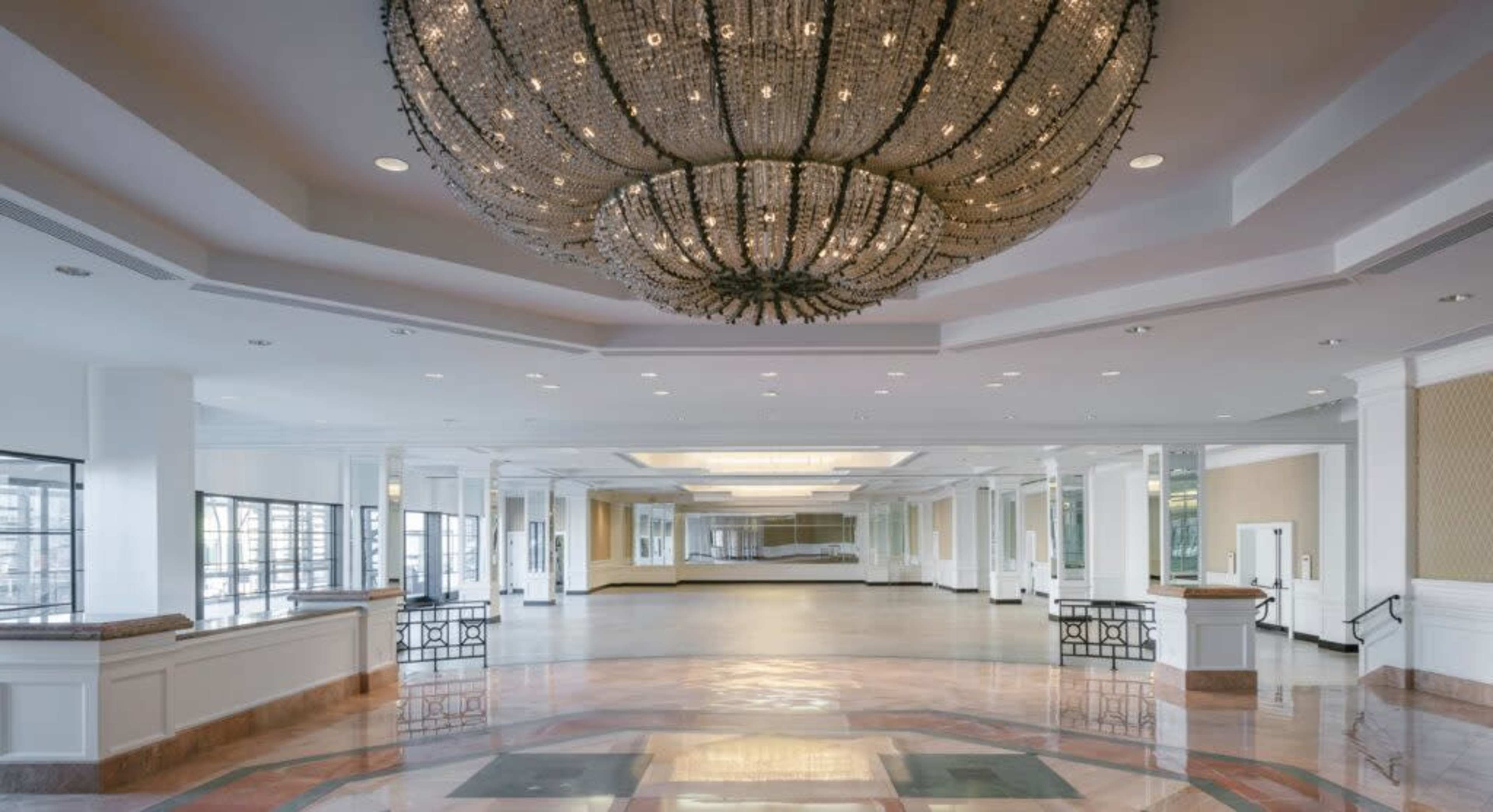 A spacious lobby area featuring a large chandelier hanging from the ceiling, with polished floors and large windows allowing natural light.