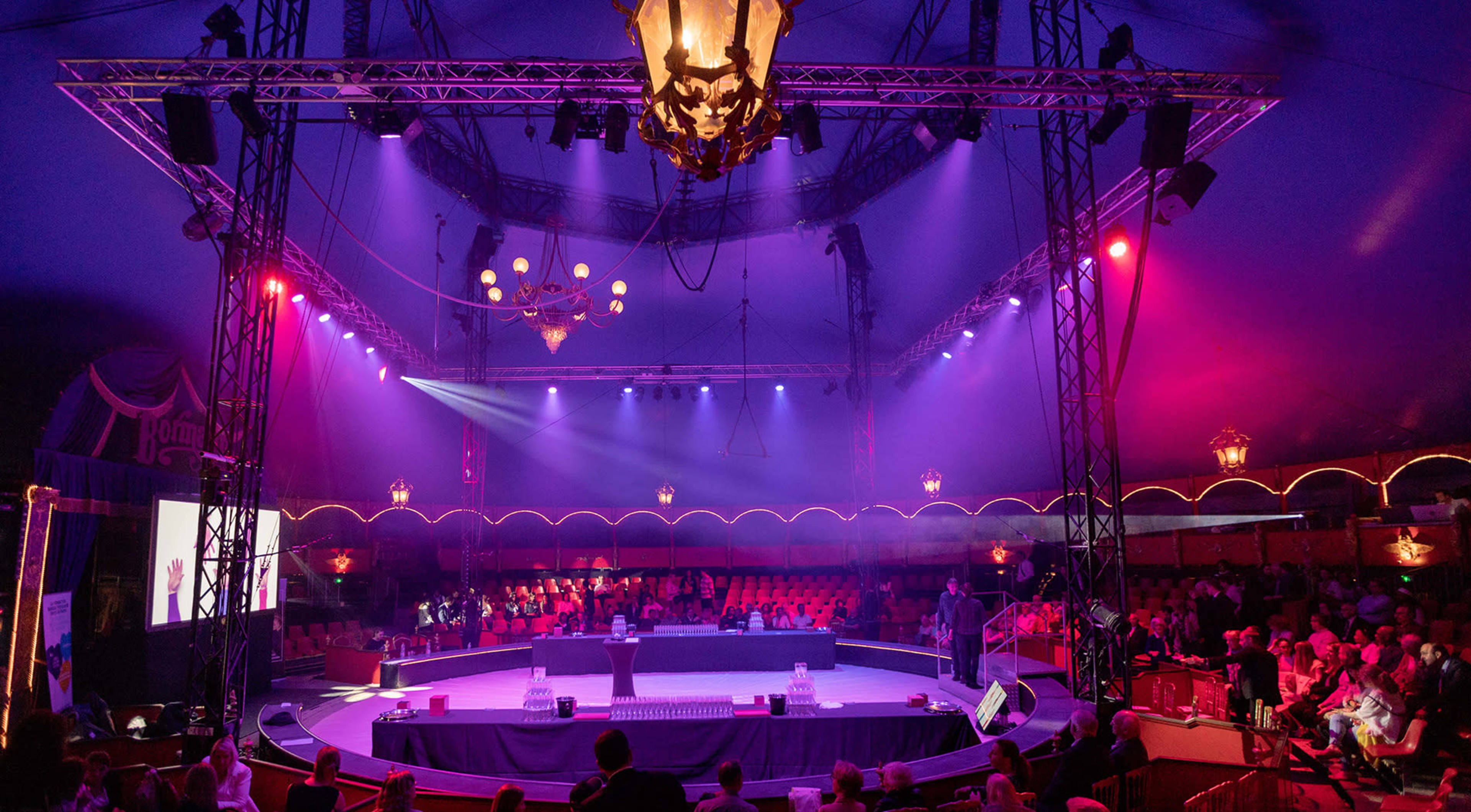 An illuminated circus stage with a circular performance area surrounded by seating for an audience.