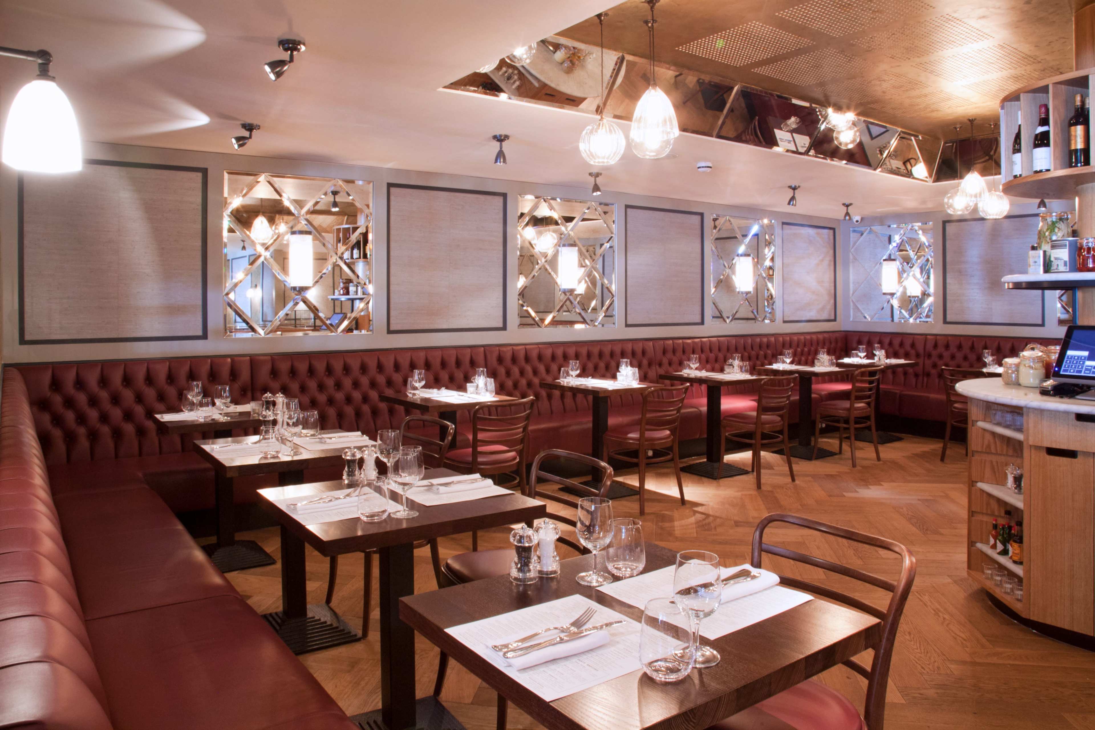 The image shows an elegantly designed restaurant interior featuring wooden tables, leather banquettes, and pendant lighting.