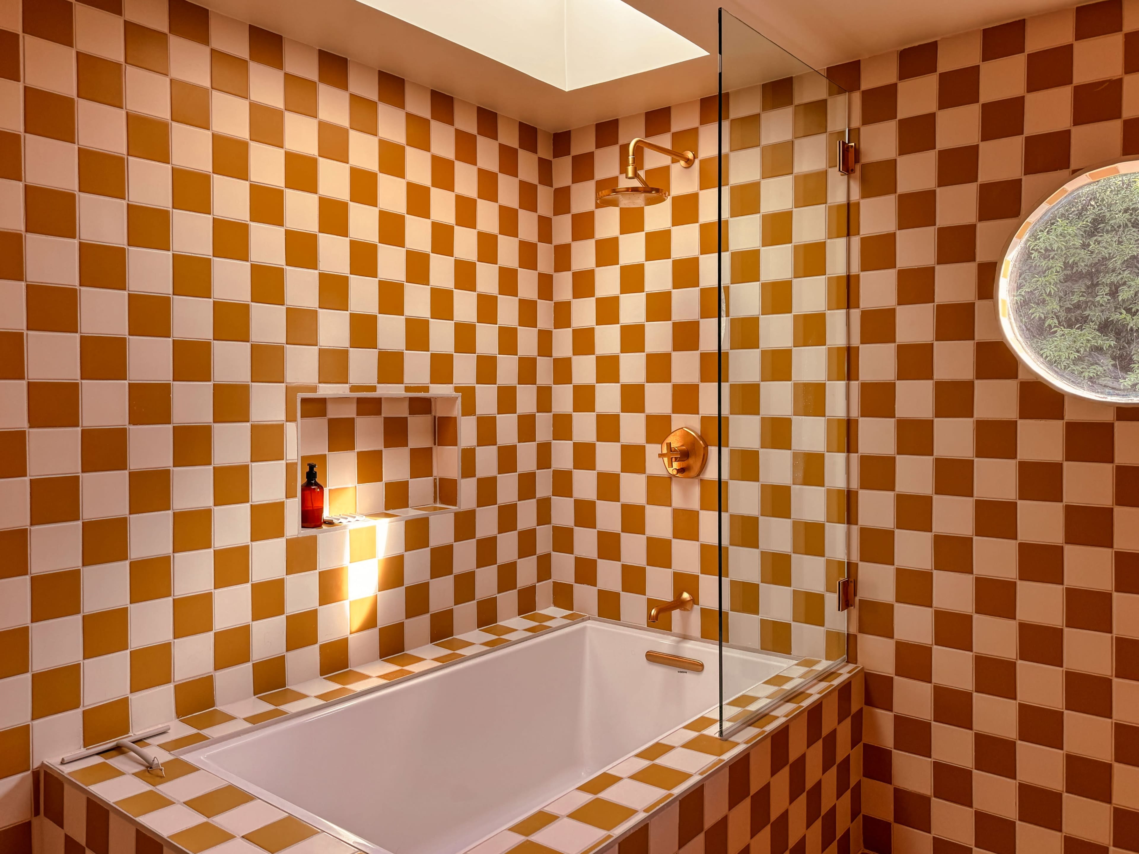The bathroom features a checkered design with orange and white tiles, showcasing a bathtub with a glass partition and a round window.
