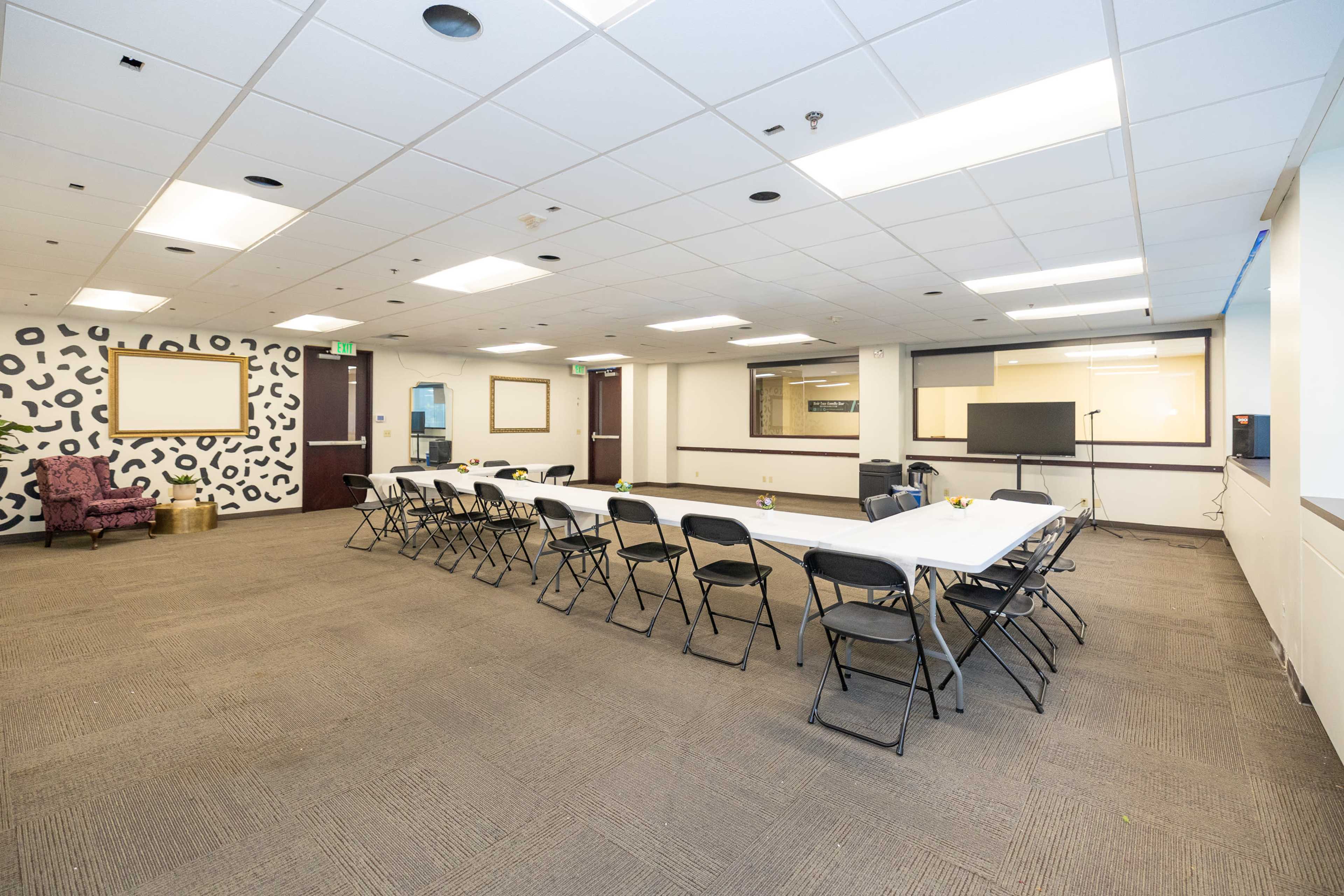 The image shows a large meeting room with a rectangular table set up for a conference, surrounded by black folding chairs, and featuring a purple armchair and decorative wall panel.