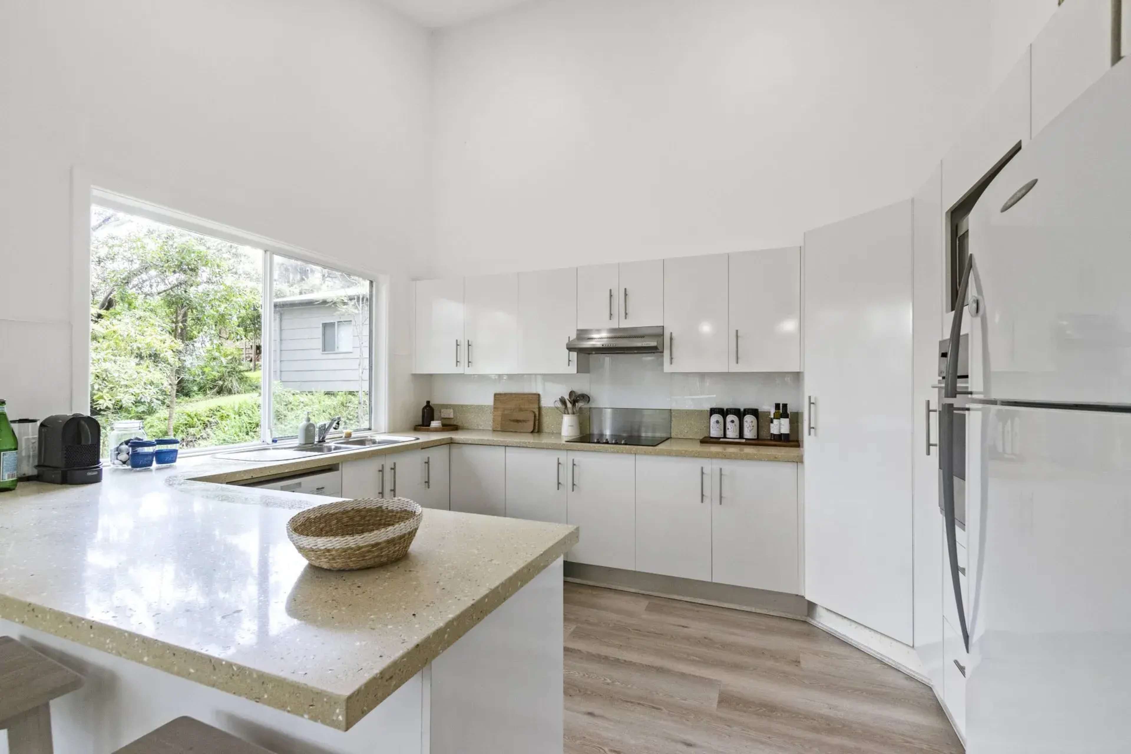 A modern kitchen features white cabinetry, a spacious countertop, and a large window that provides natural light and a view of the outdoors.