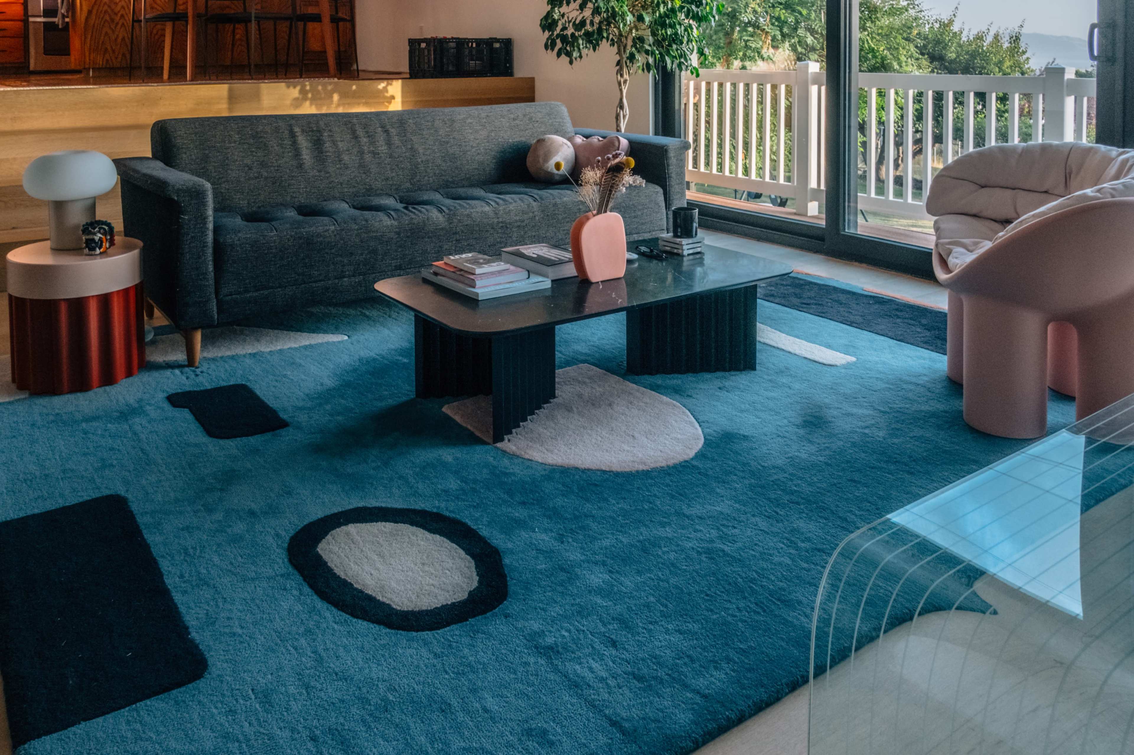 The image shows a modern living room featuring a gray sofa, a coffee table, and a colorful area rug with geometric patterns.