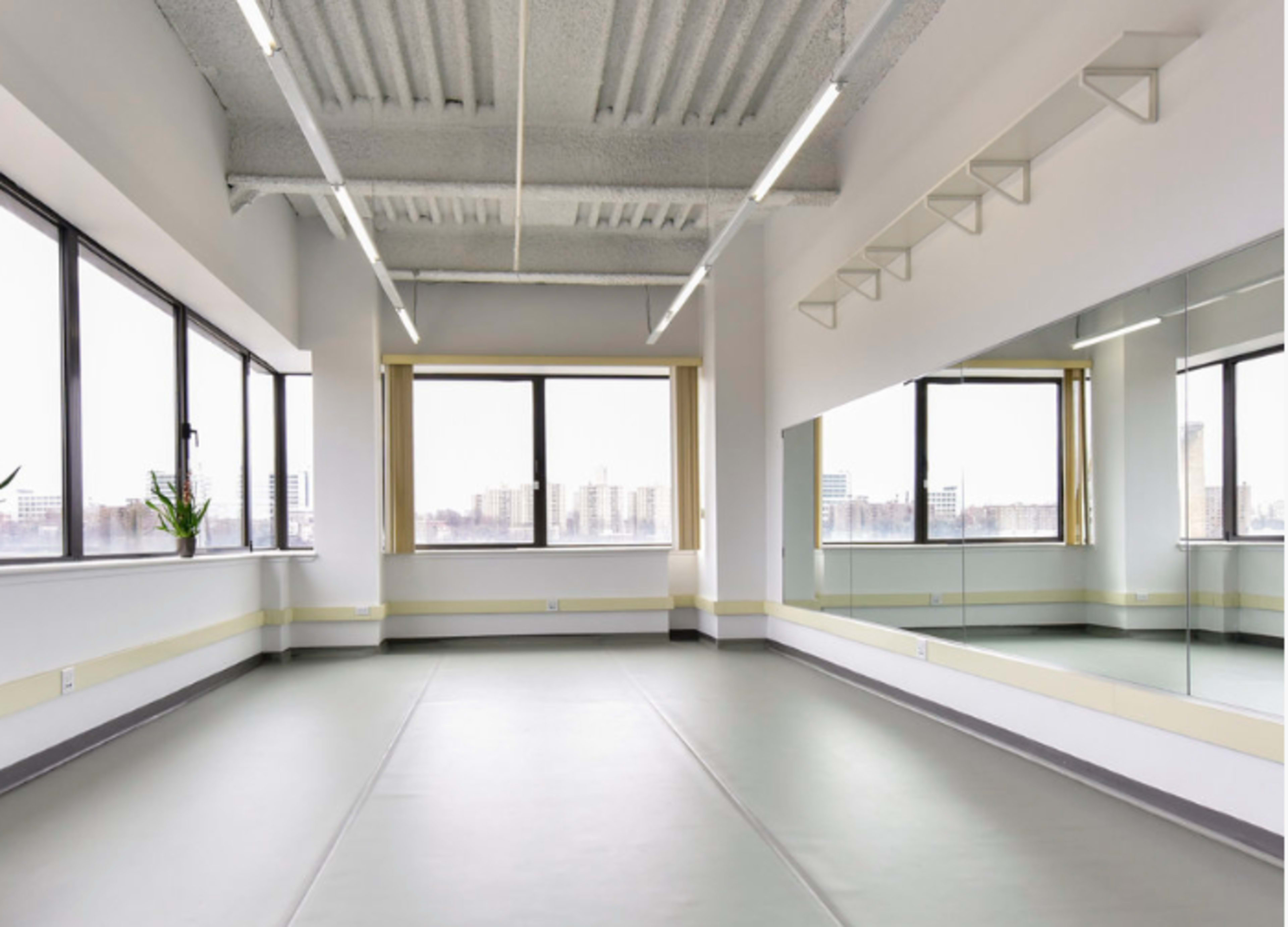 A spacious, minimalist studio with large windows, natural light, and a mirrored wall.