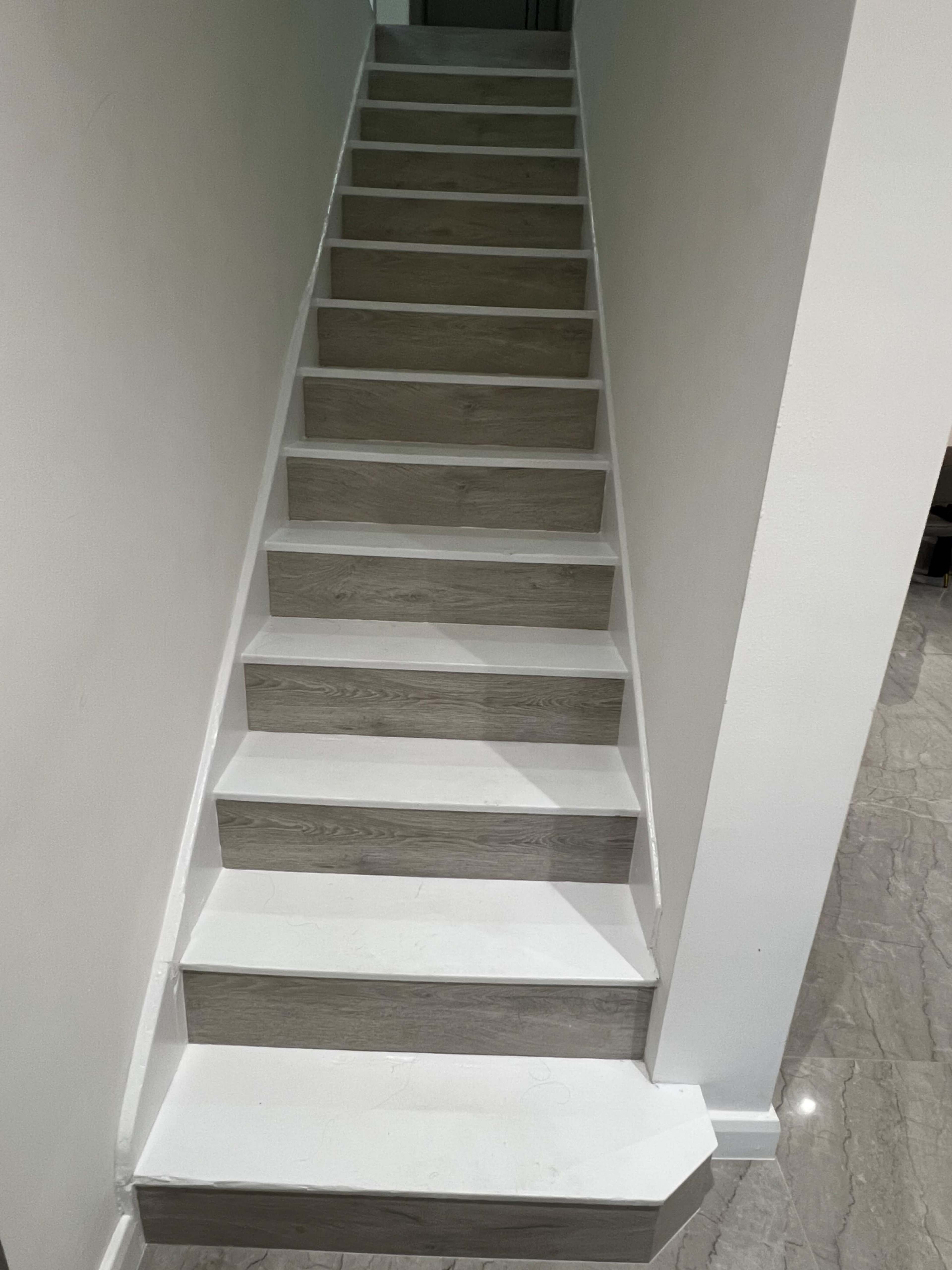 A staircase with light-colored wooden steps and white risers ascends against a plain white wall.
