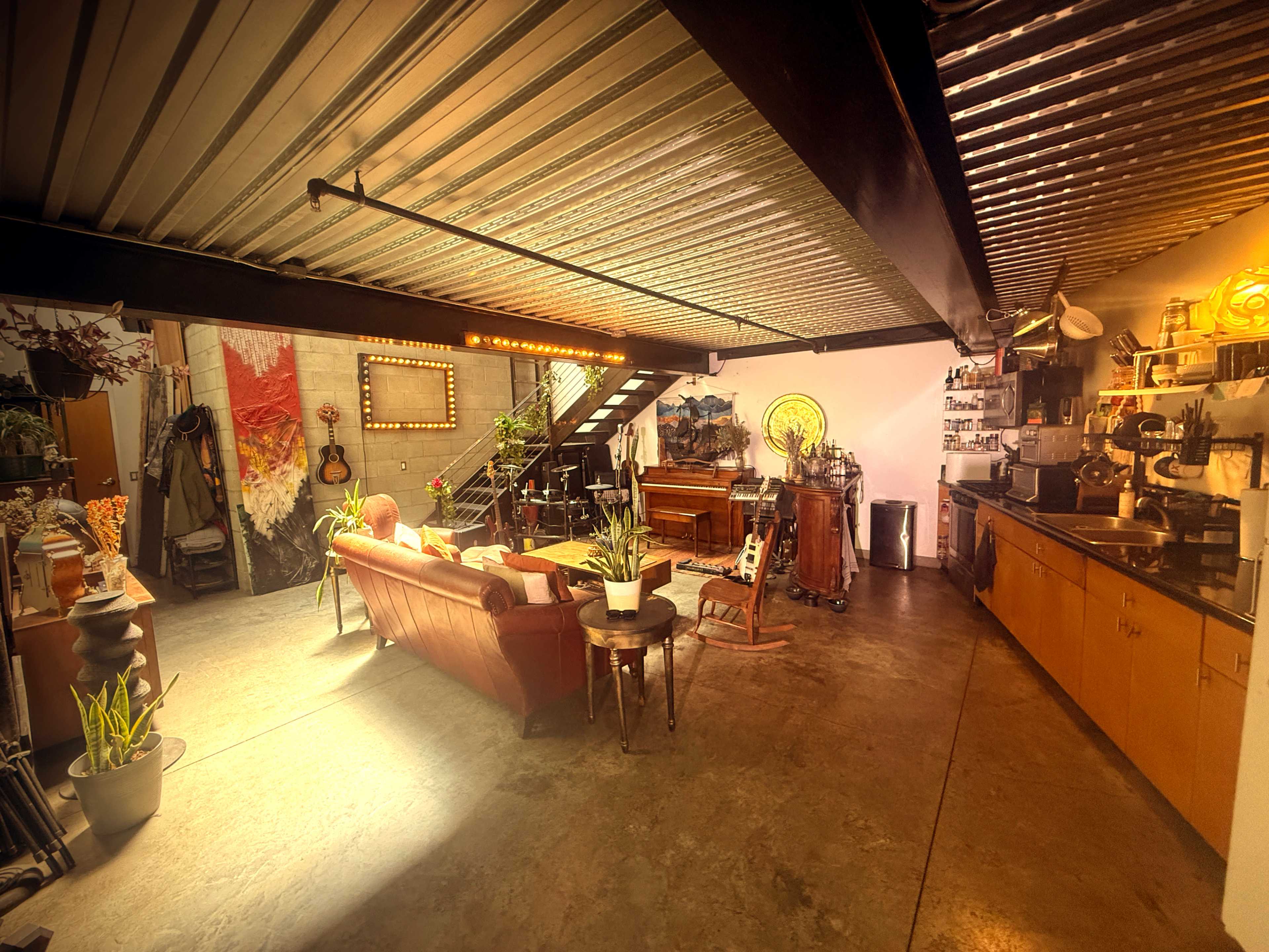 The image shows an open living space featuring a seating area with a sofa, a staircase leading to an upper level, and a kitchen area with wooden cabinetry.