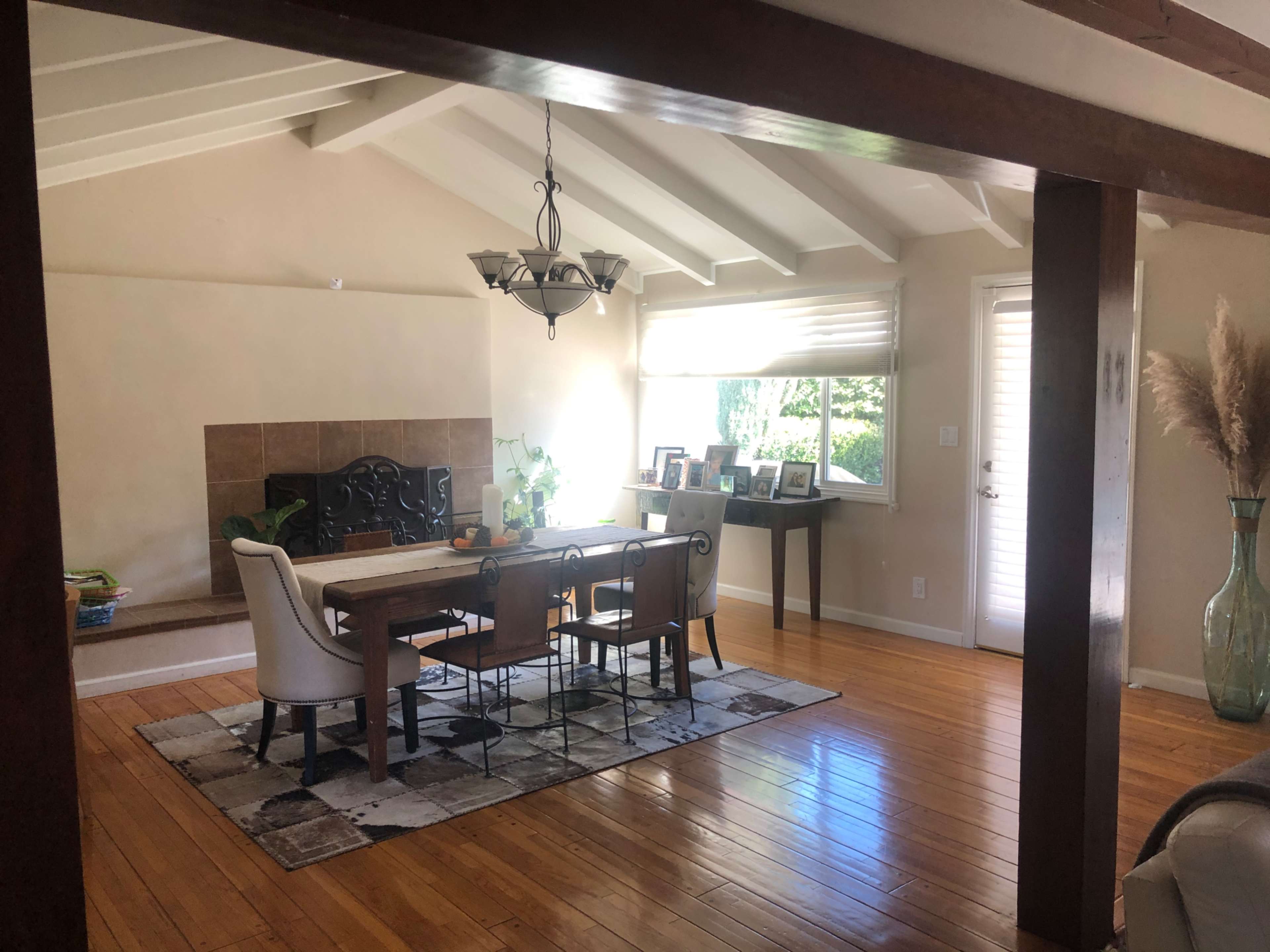 A dining area with a wooden table, four chairs, and a decorative vase, set against a backdrop of wooden beams and large windows.