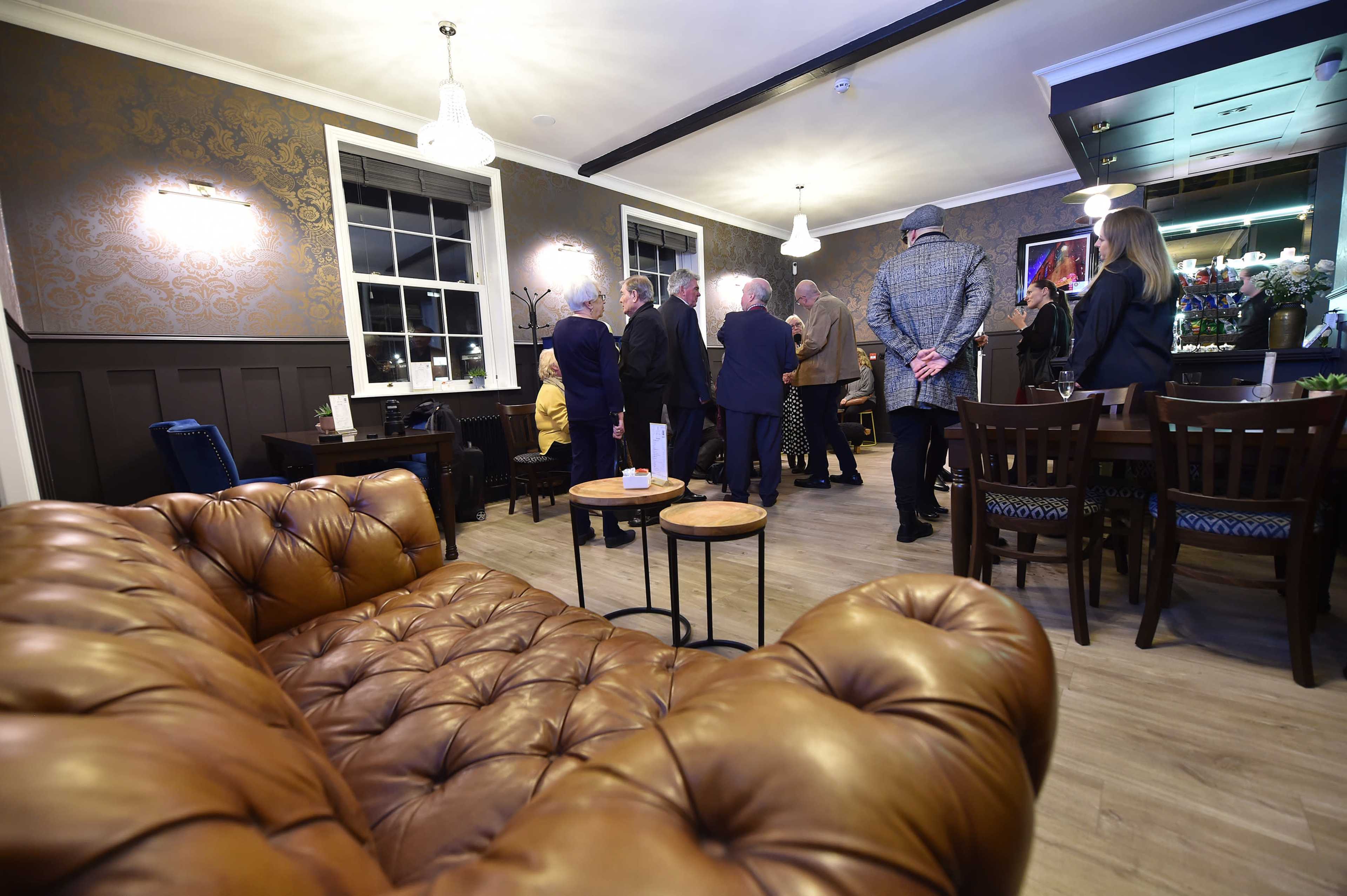 A group of people converses in a warmly lit lounge, with leather upholstery and decorative walls.