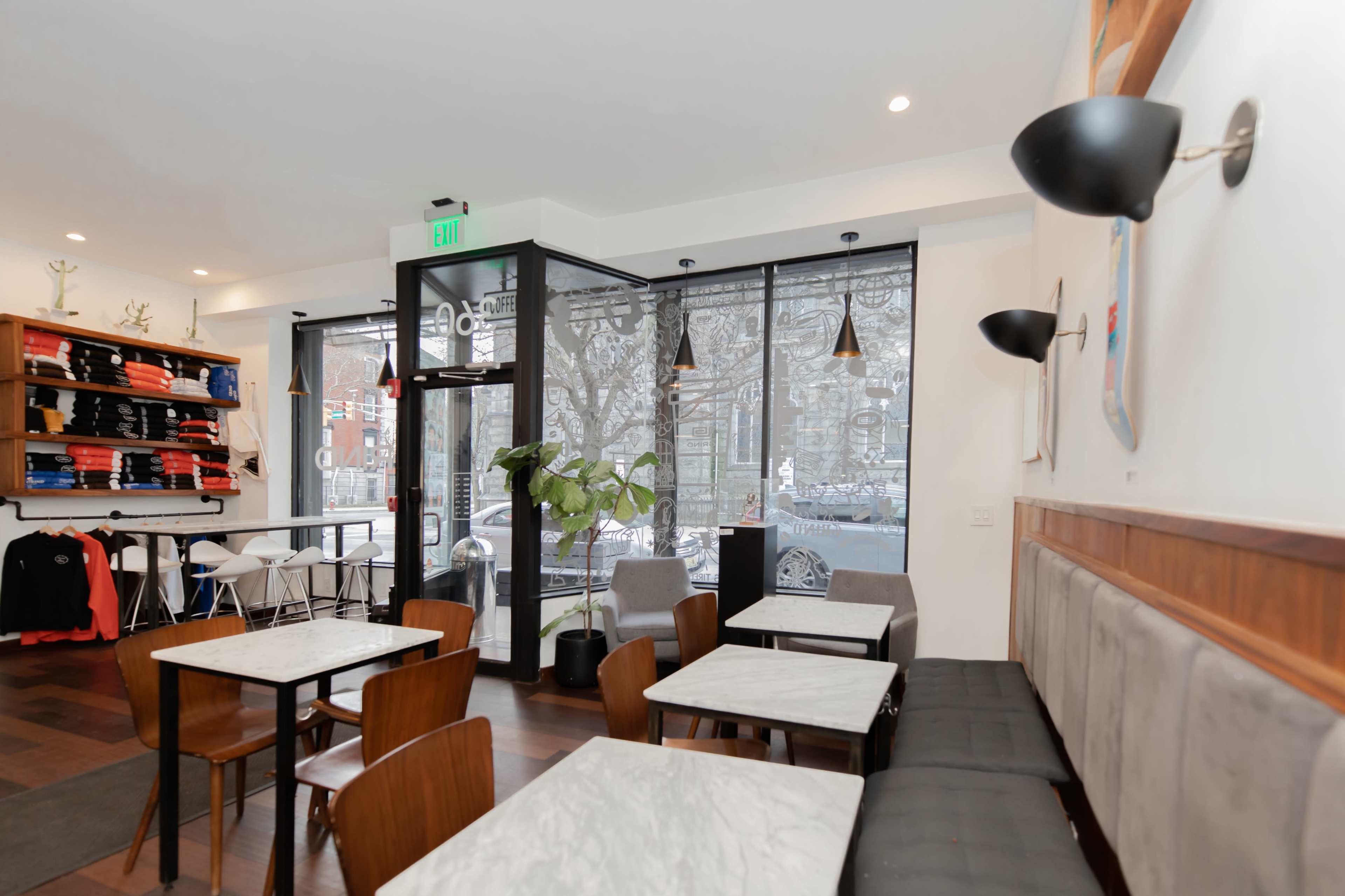 A modern café interior with wooden tables, chairs, and a large window facing the street.
