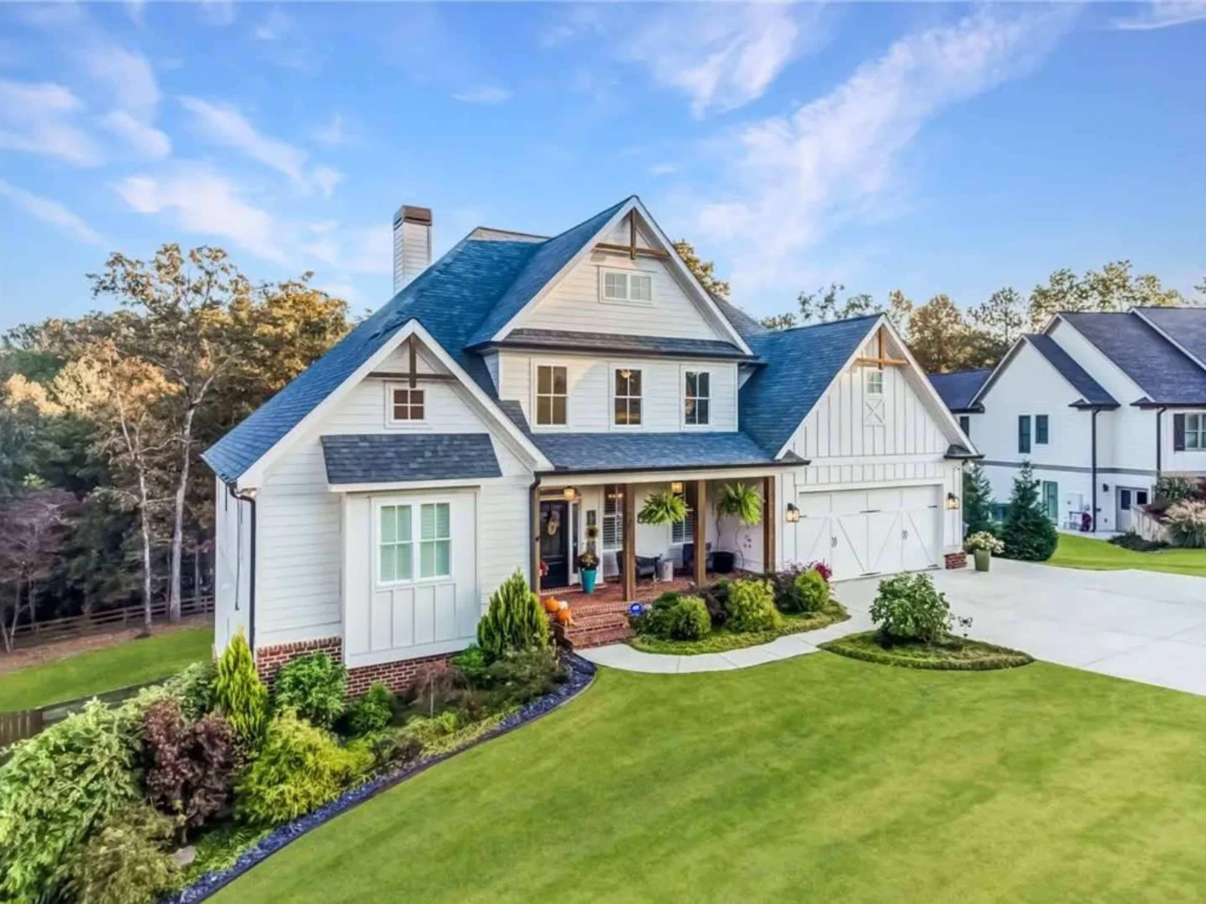 A two-story house with a gabled roof and a welcoming front porch is surrounded by manicured lawns and landscaped gardens.