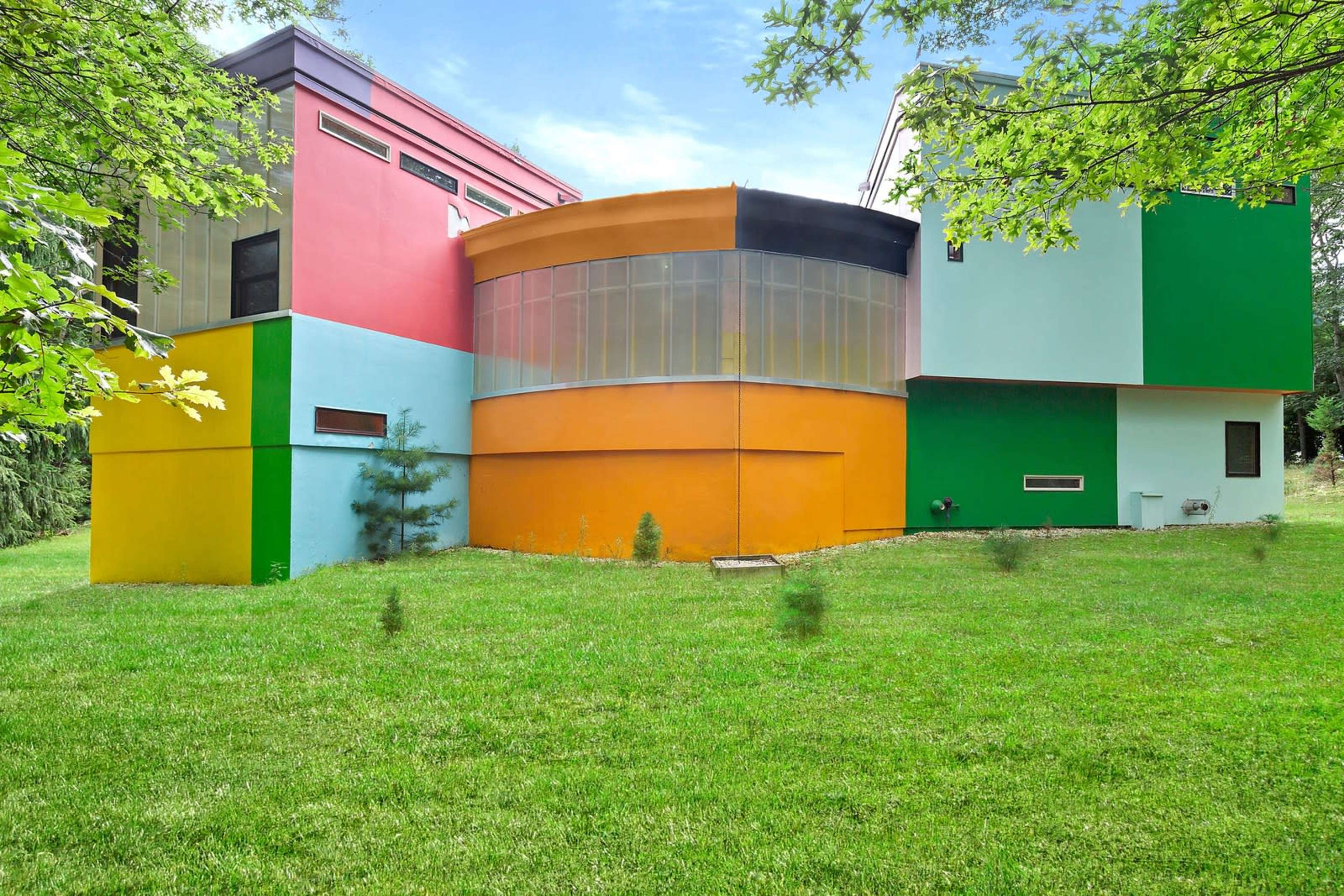 The image shows a modern architectural structure with vibrant, multicolored walls set against a grassy lawn.