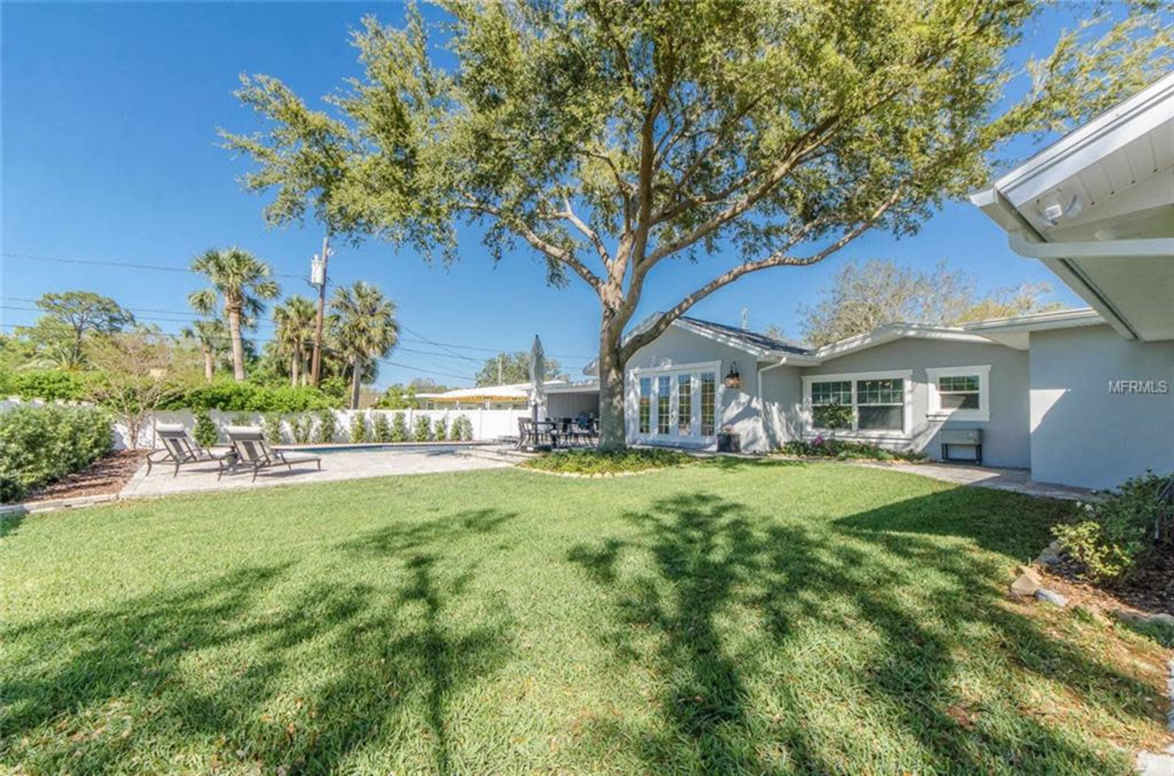 A spacious backyard with a well-manicured lawn, patio area, and a large tree.