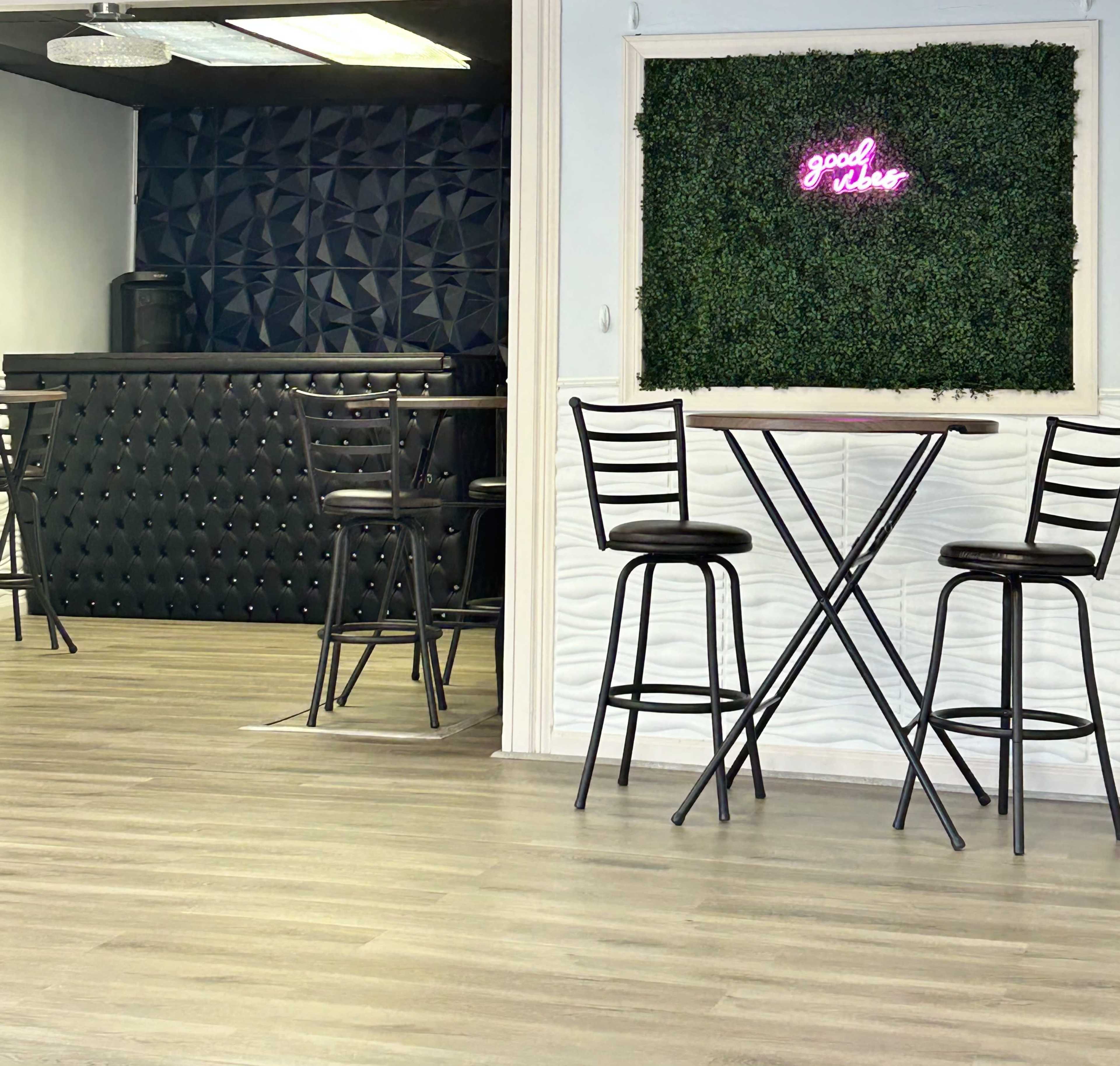 A modern interior with a bar area featuring a textured black wall, two tall bar stools, and a neon sign on a green wall that reads "good vibes."