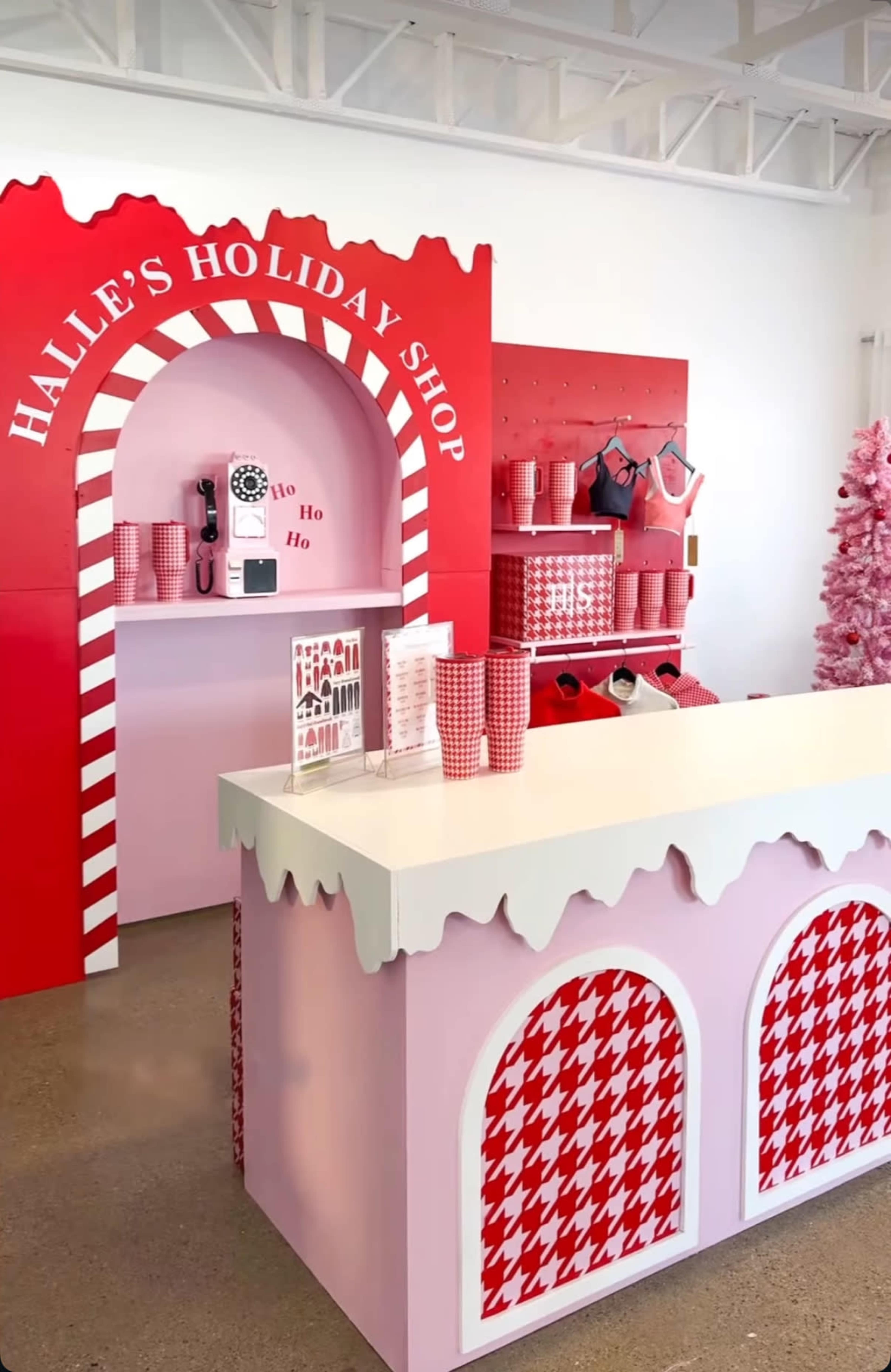 The image shows a brightly decorated holiday shop with a red and white theme, featuring candy cane elements, a pink counter, and festive displays.