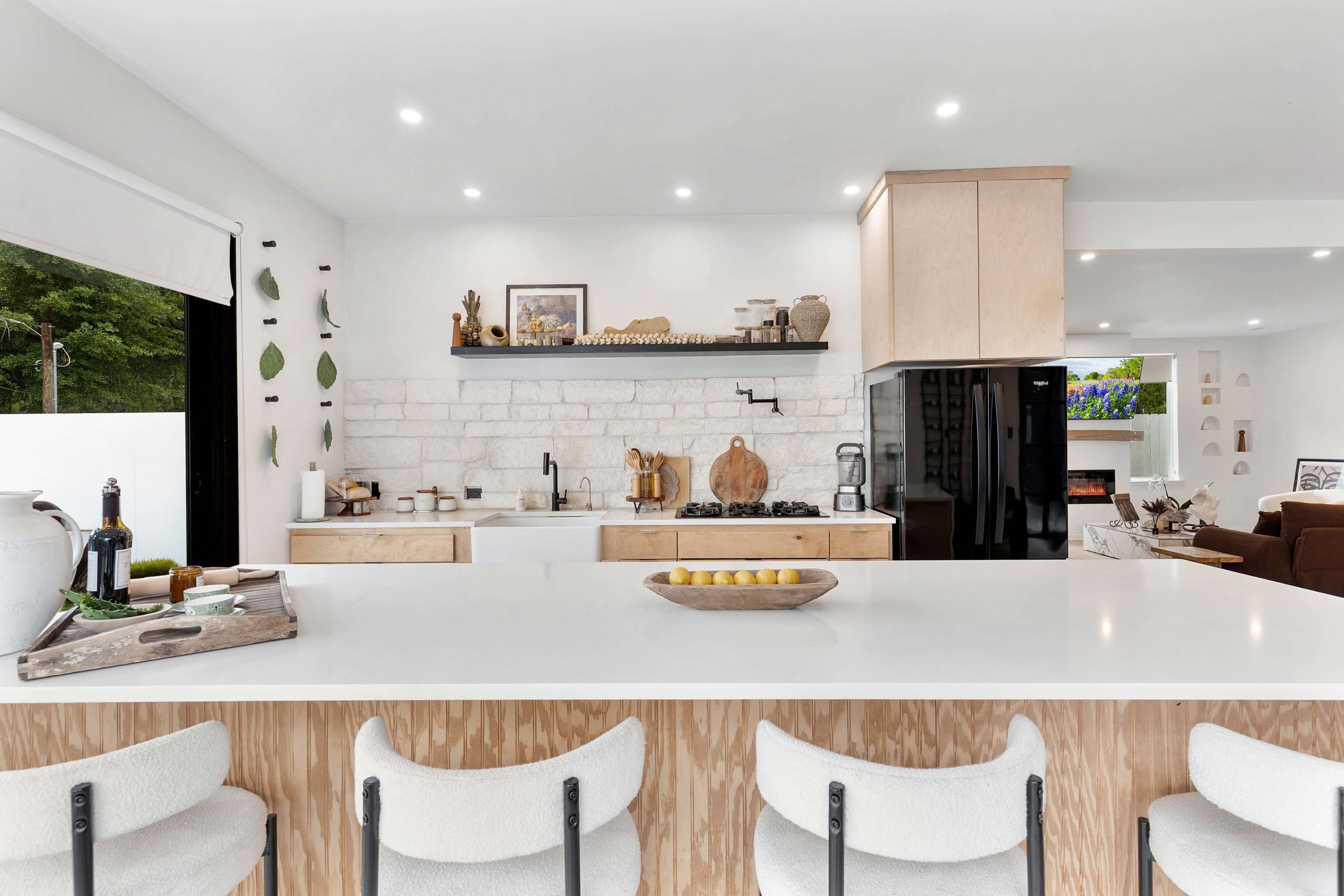 The modern kitchen features a large white island with bar stools, a stone accent wall, wooden cabinetry, and black appliances.
