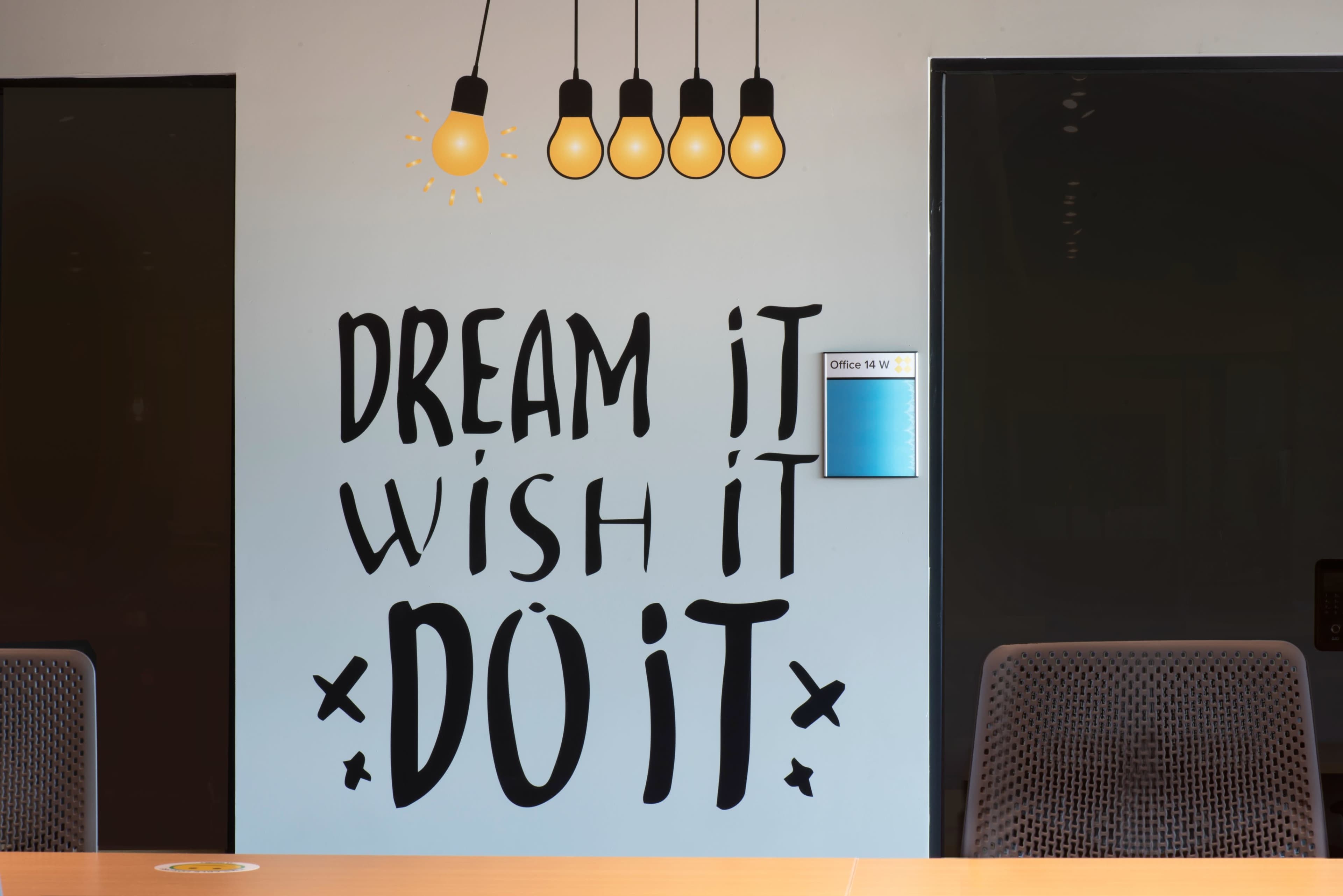 A wall with the motivational phrase "DREAM IT WISH IT DO IT" in large letters, illuminated by four hanging light bulbs above a table and a door on the right.
