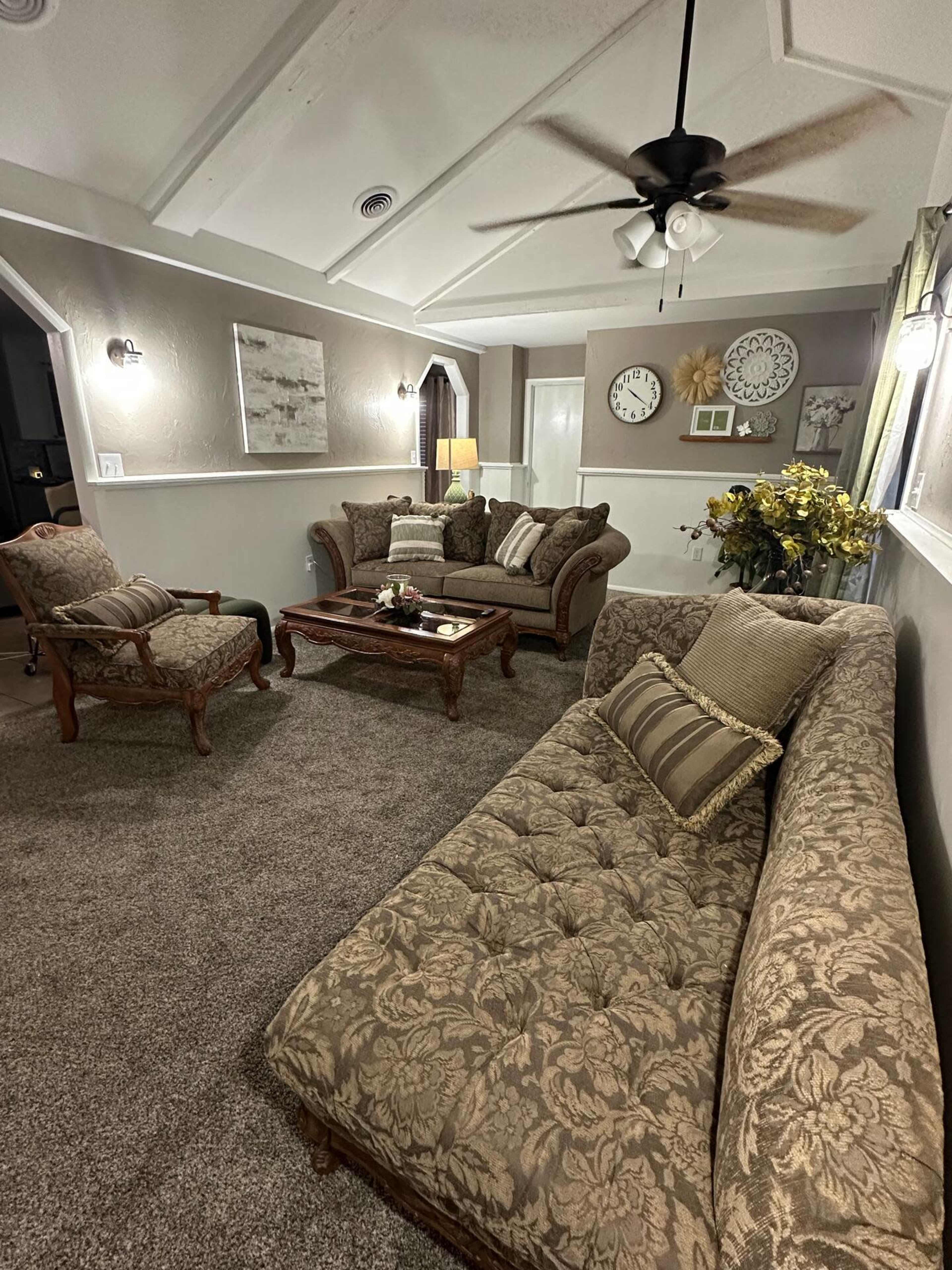 The image shows a living room with two upholstered sofas and a coffee table, surrounded by decorative elements and a ceiling fan.