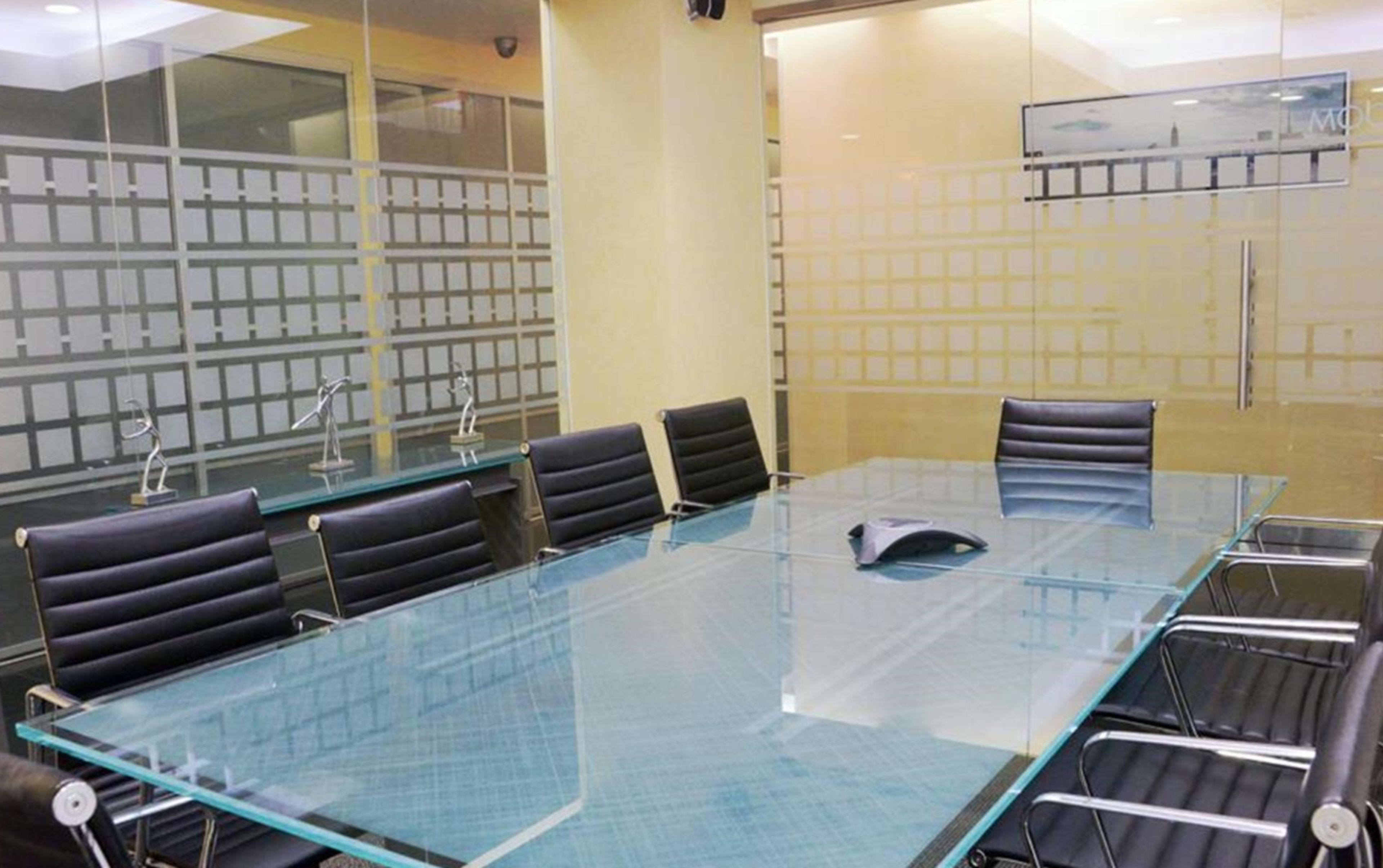A modern conference room features a large glass table surrounded by black leather chairs.