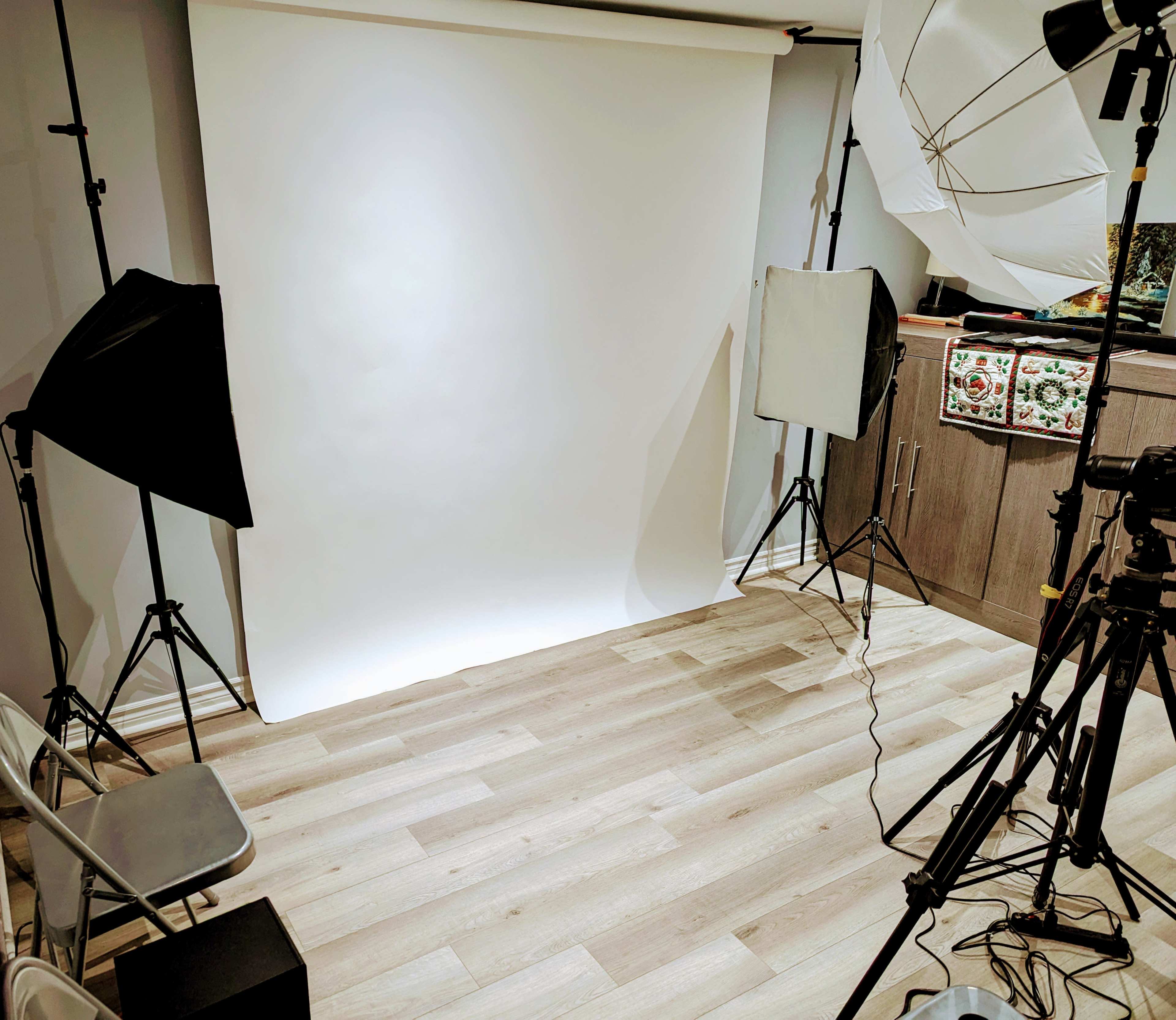 A photography studio setup with a white backdrop, two light stands, and a camera on a tripod.