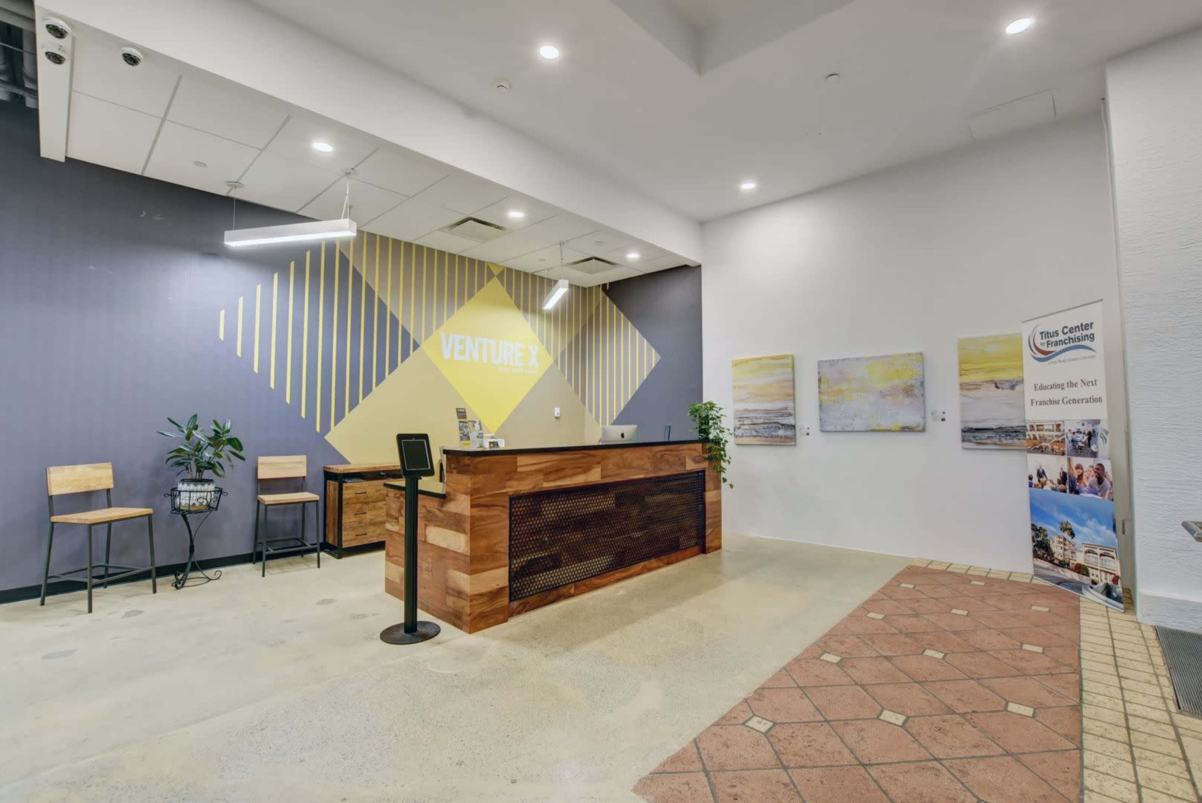 A modern reception area with a wooden front desk, two bar-style stools, and decorative artwork on the walls.