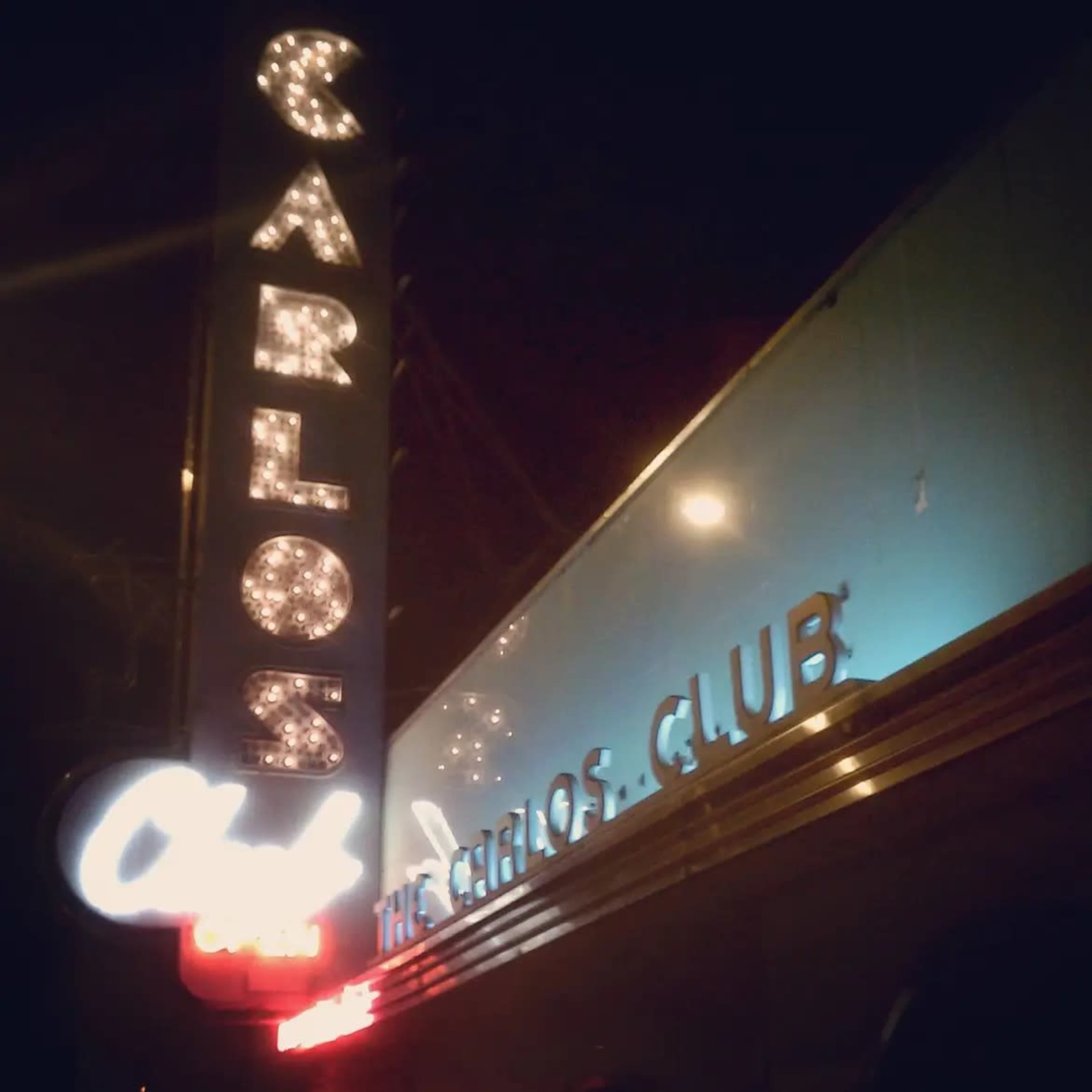 The illuminated marquee of Carlos Club displays its name against a night sky.