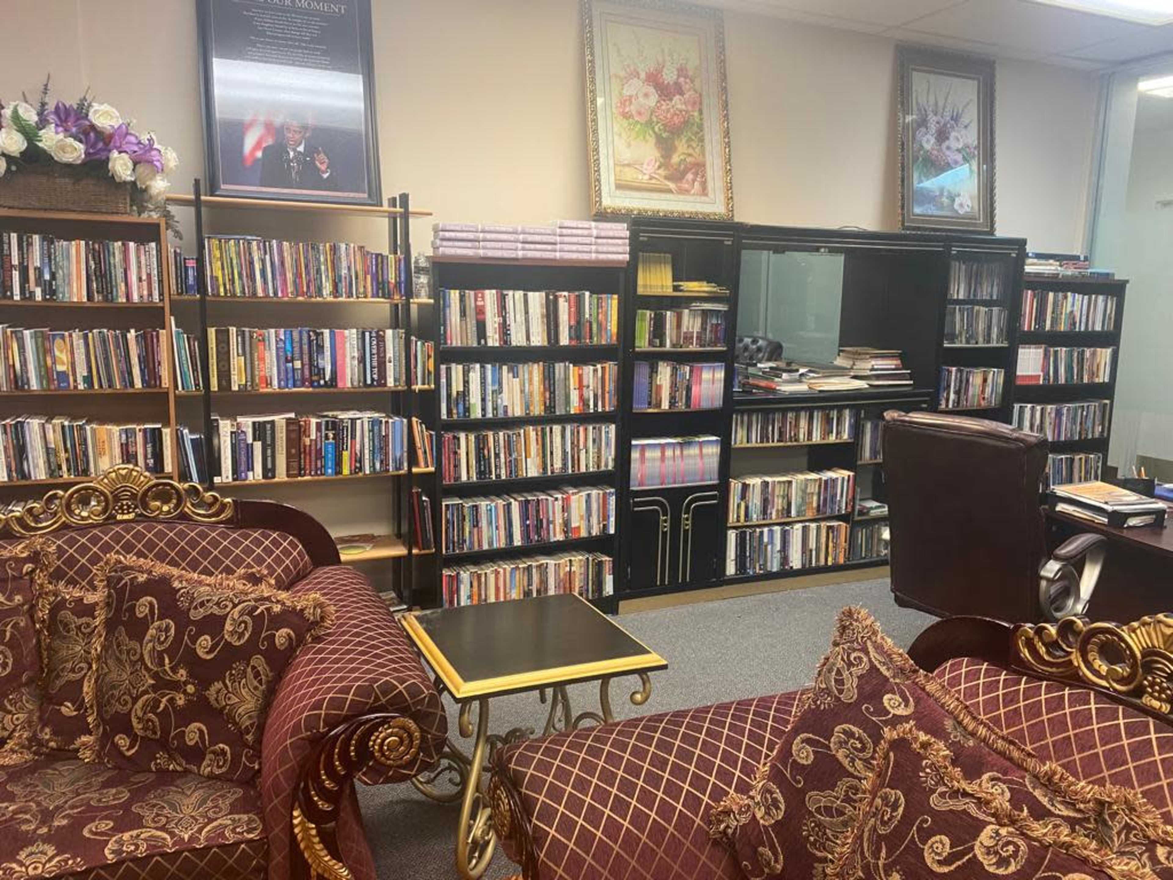 A cozy reading area with two ornate couches, a small table, and bookshelves filled with books and DVDs along the walls.