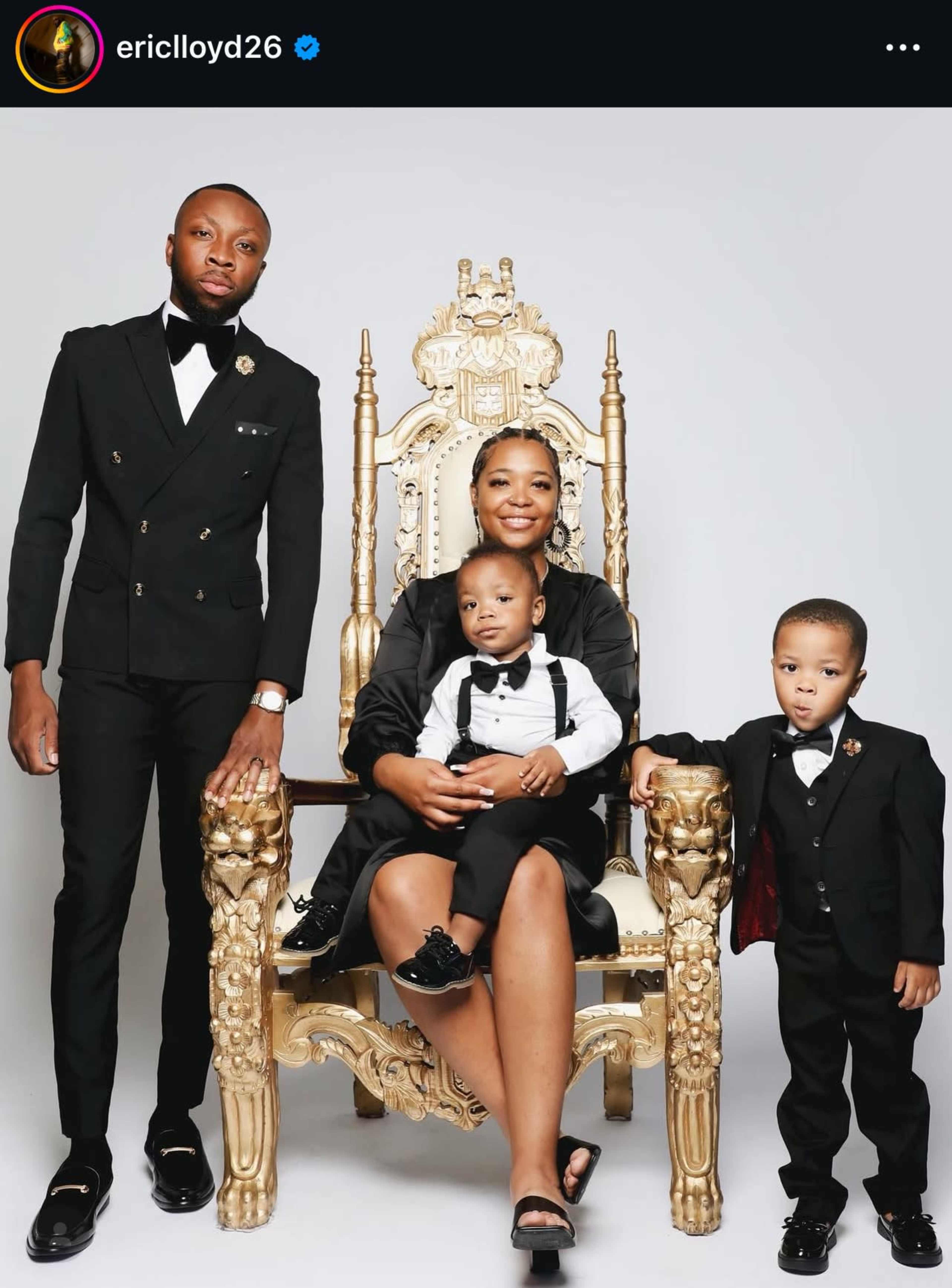 A family poses together on a gold throne, dressed in formal attire, with two young boys standing beside their seated mother.