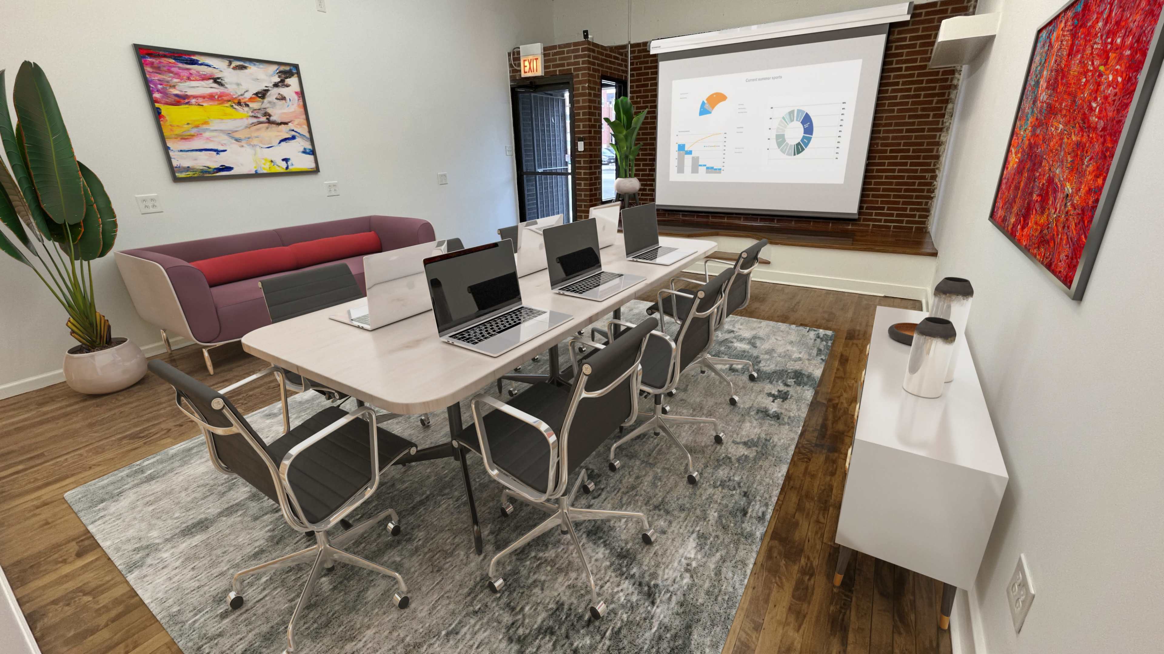 A modern conference room features a long table with multiple laptops, a large screen displaying graphs, and contemporary decor, including artwork and plants.