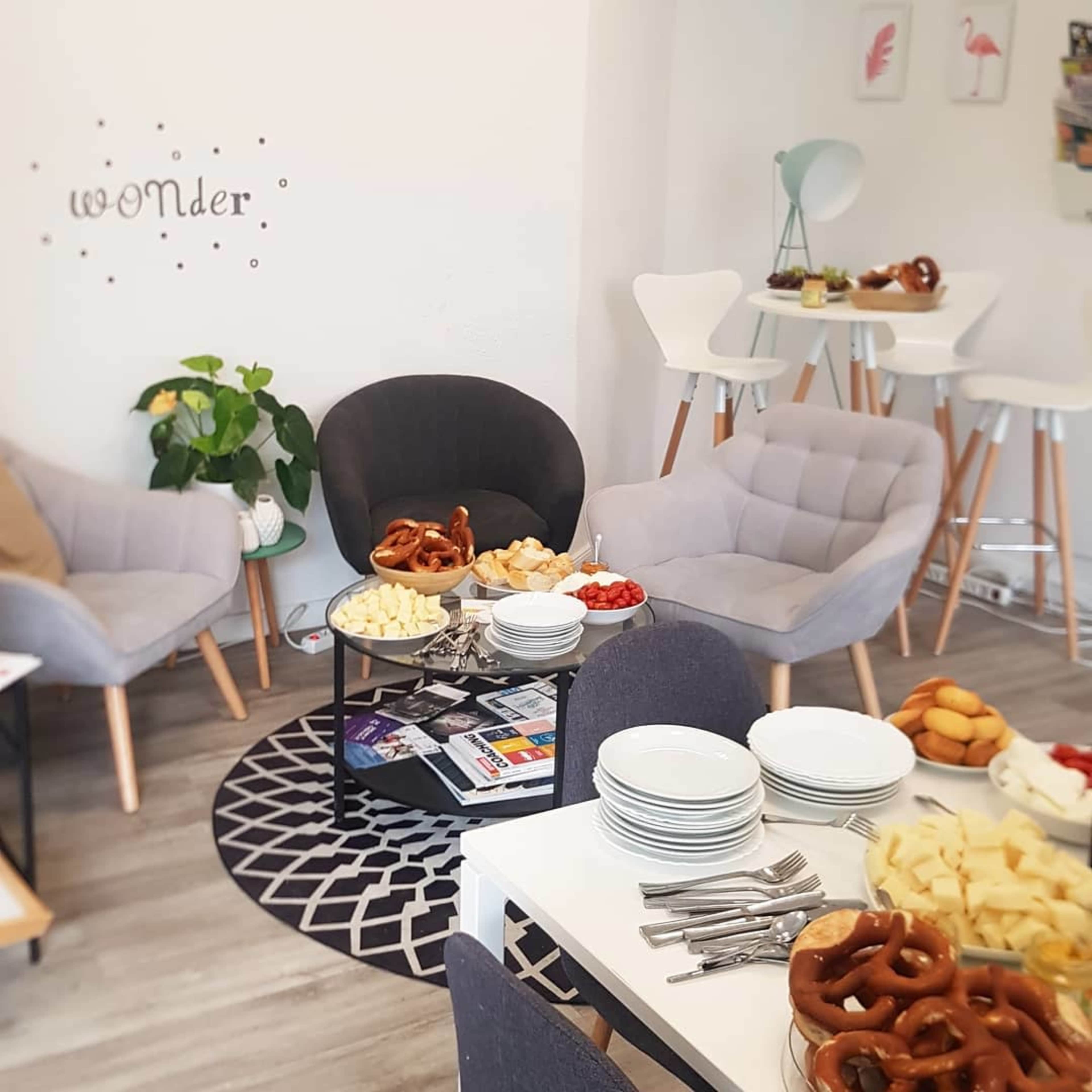 A cozy gathering space features gray armchairs and a white dining table adorned with plates of sliced cheese, fruit, and pretzels.