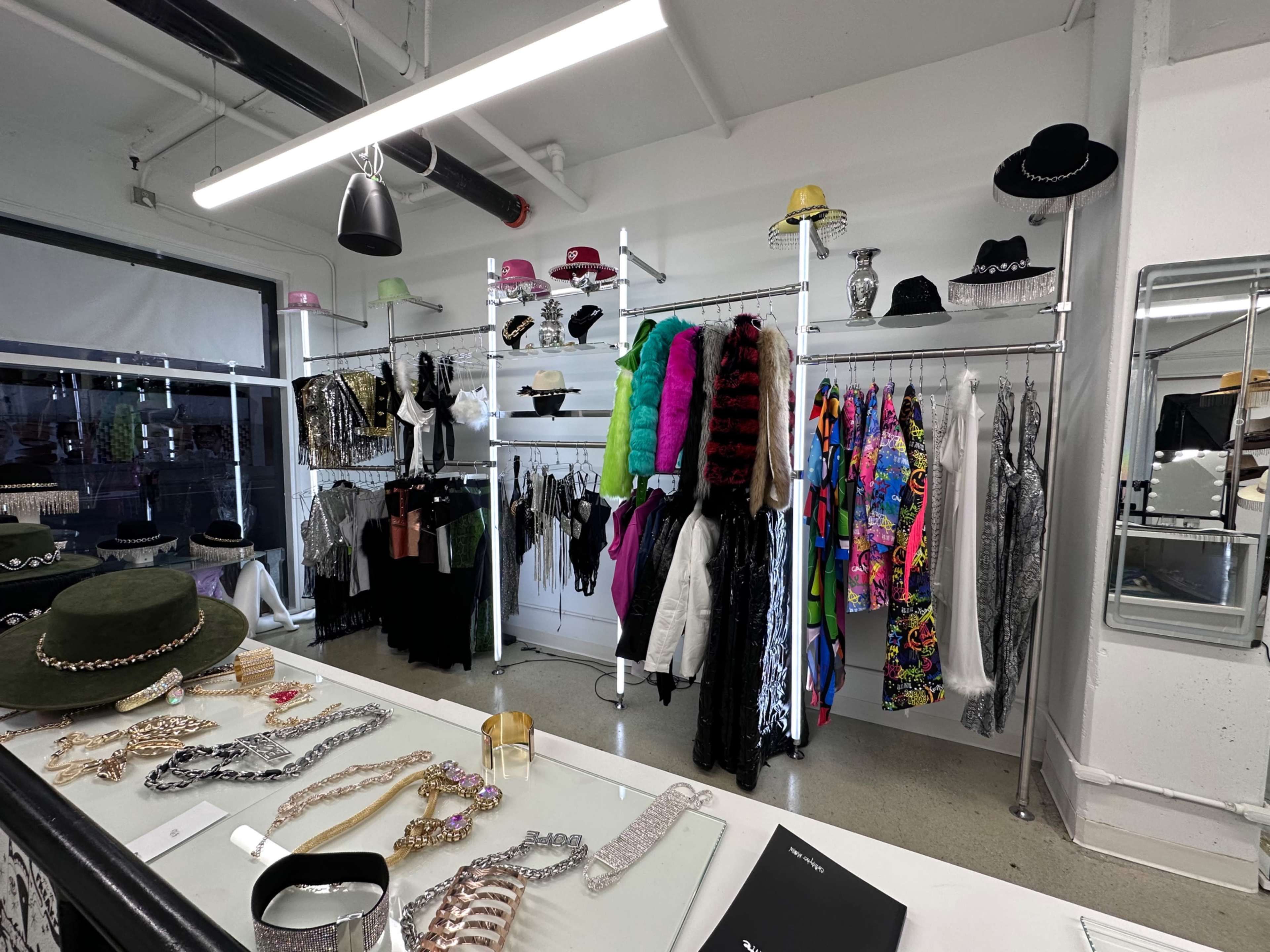 The image shows a clothing store interior featuring a display of colorful apparel, hats, and accessories organized on metal racks and a glass counter.