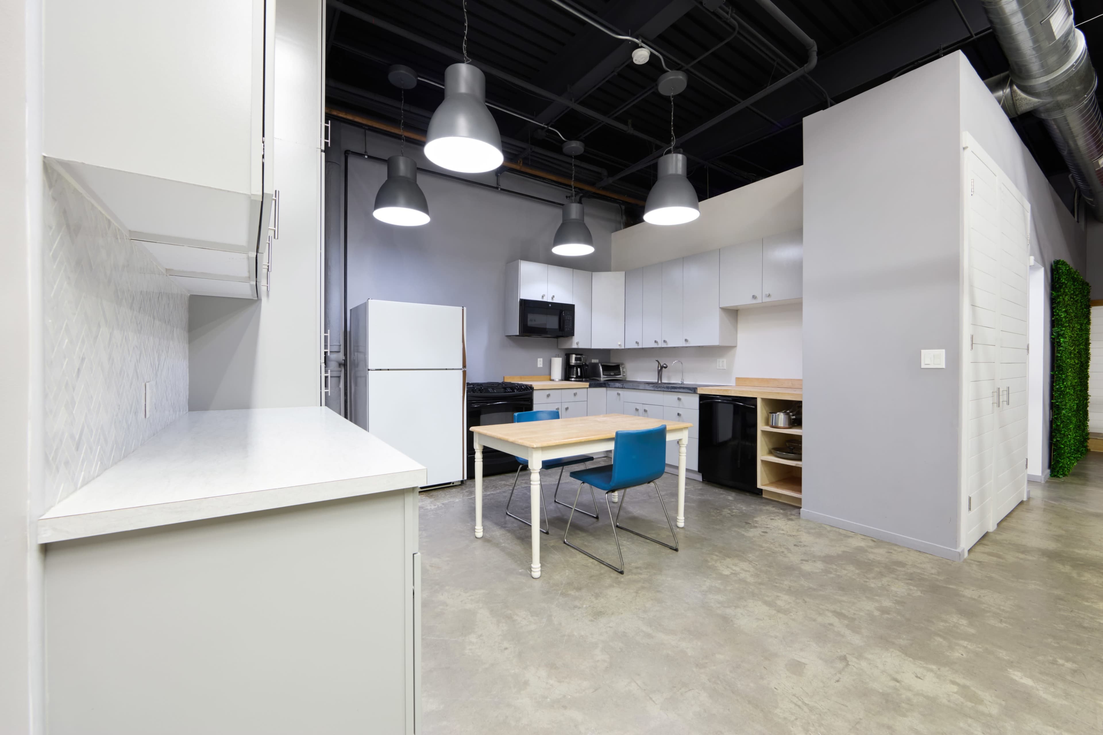 The image shows a modern kitchen area with a table and chairs, appliances, and pendant lighting.