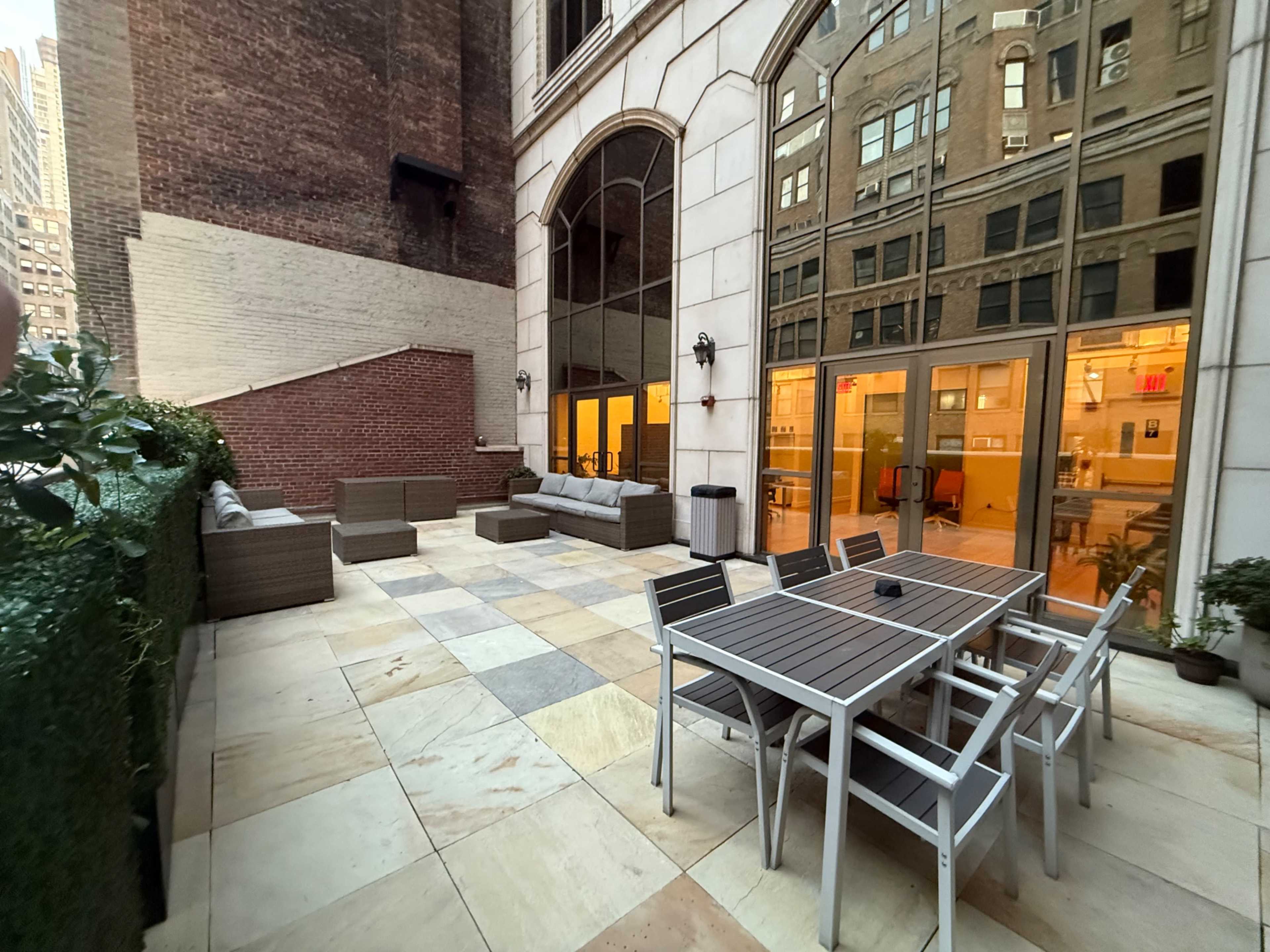 The image shows a spacious outdoor patio area featuring a seating arrangement with couches and a dining table surrounded by a mix of tile and stone flooring.