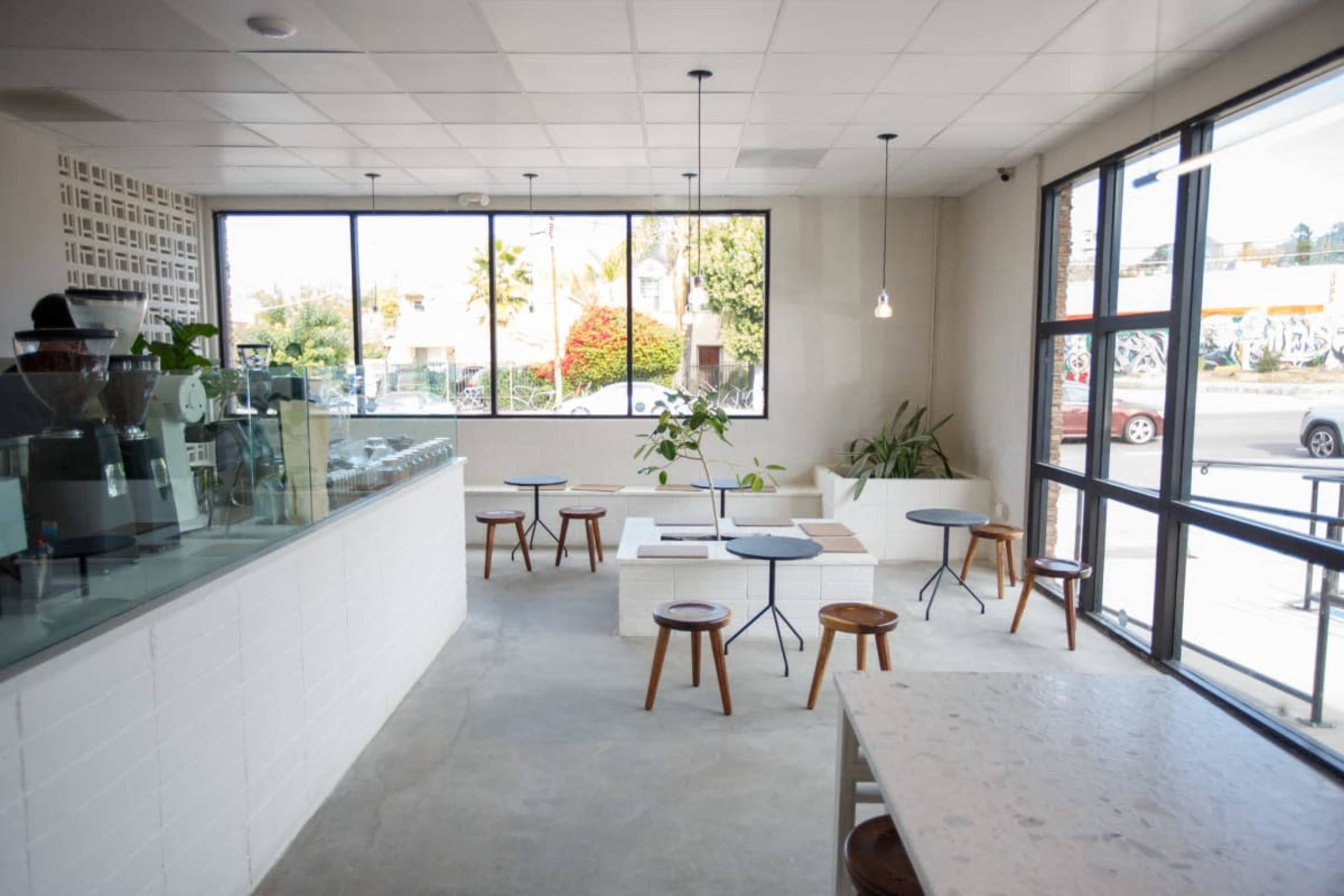 A modern café interior with a spacious layout, featuring a counter on the left, small tables with chairs, and large windows overlooking the street.