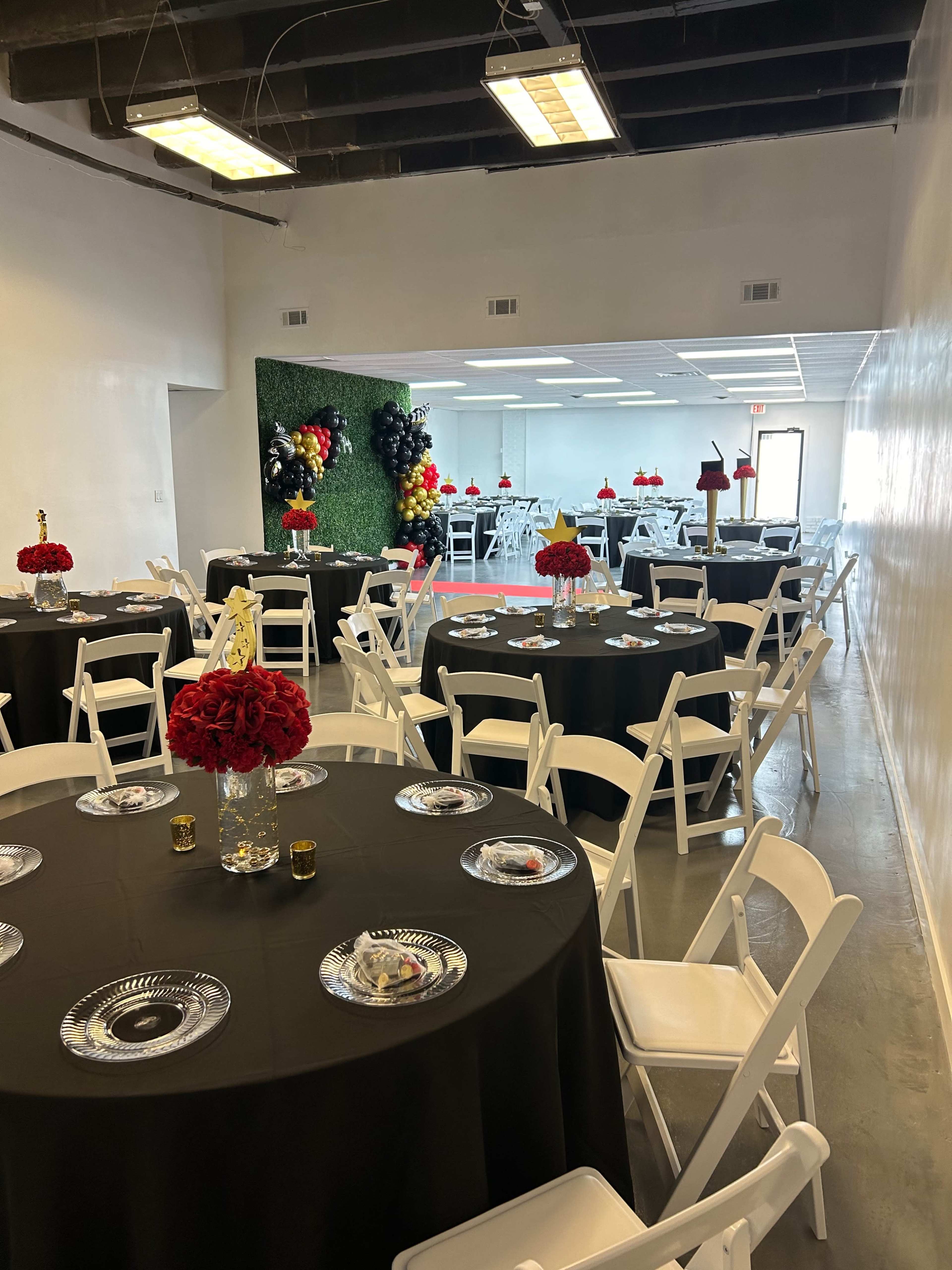 The image features a banquet hall set up with black tablecloths, white chairs, and centerpieces of red flowers, ready for an event.