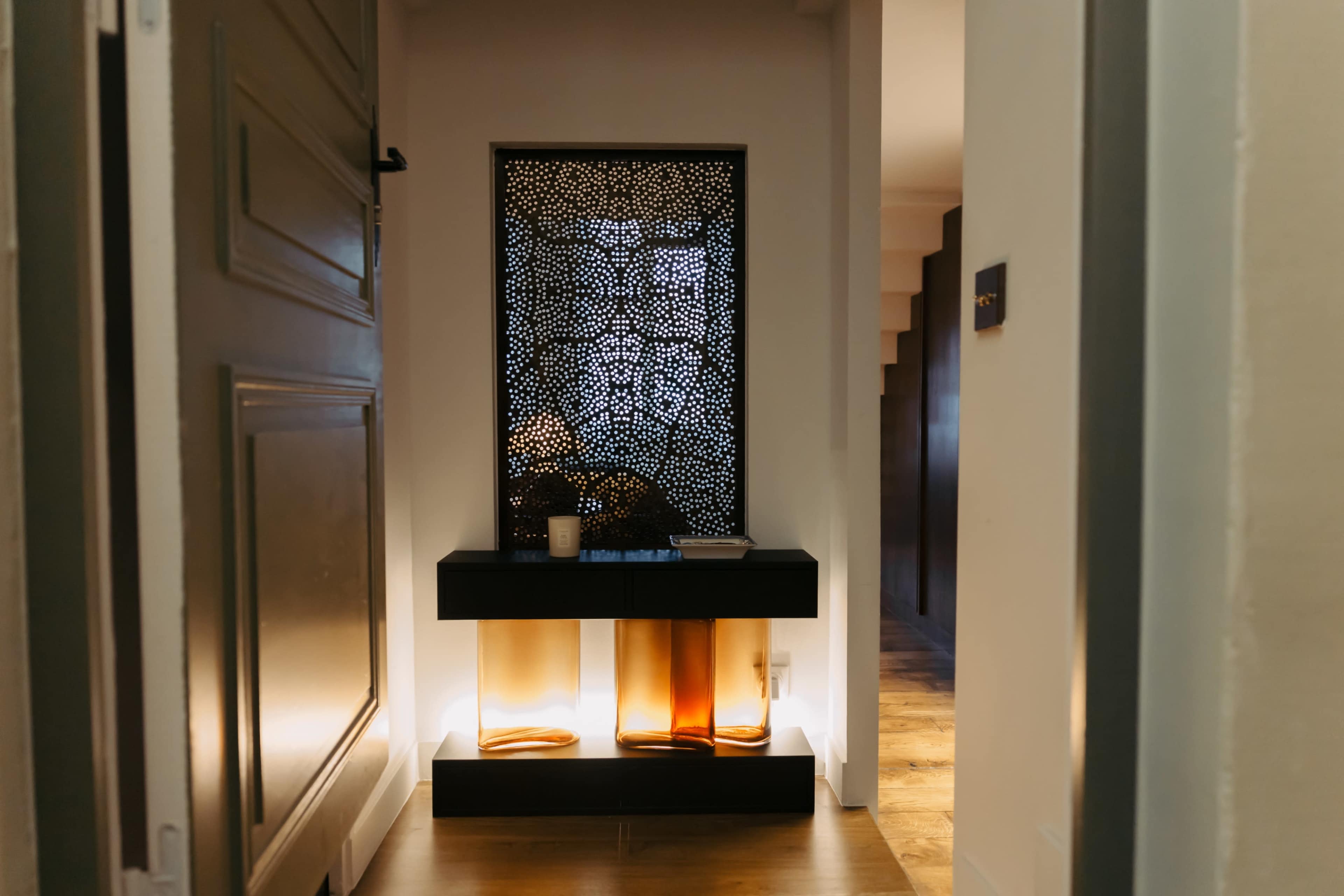 The image shows a narrow hallway with a decorative screen and a console table featuring amber and brown glass elements.