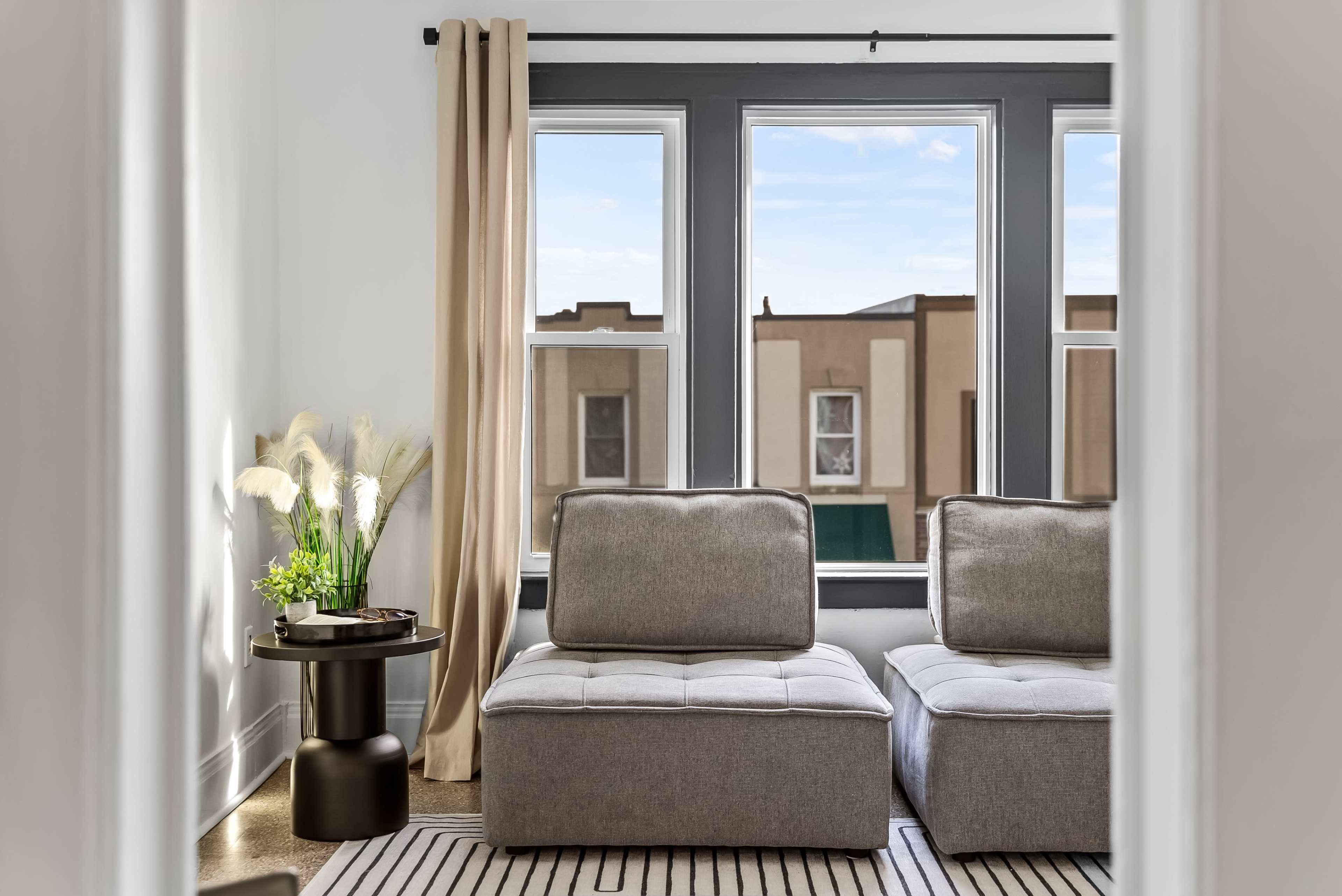 A living room with two gray upholstered sofas facing a window, accompanied by a small round table and a vase of plants.