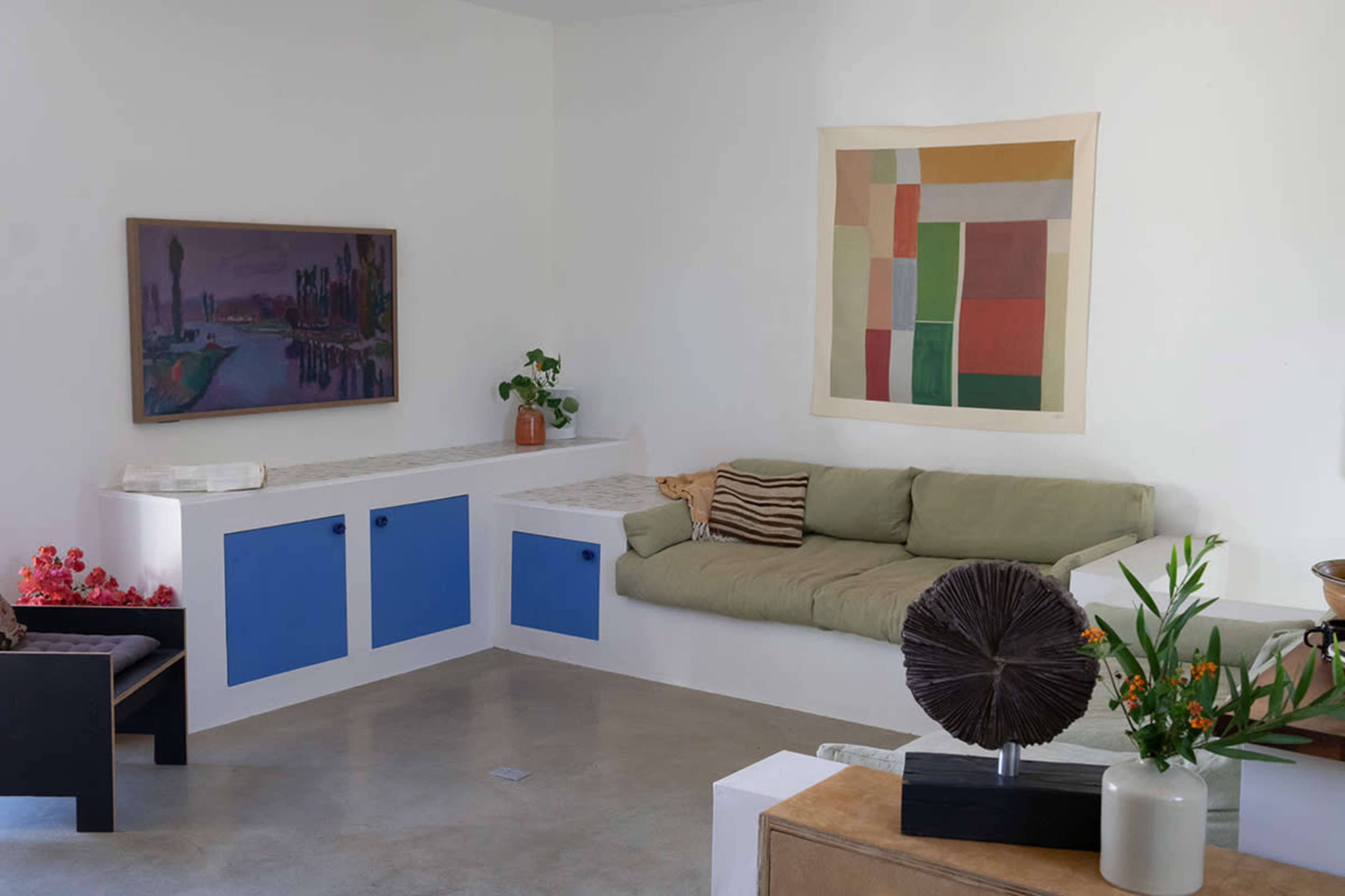 A minimalist interior space features a green sofa, abstract artwork on the walls, and decorative plants on a side table.