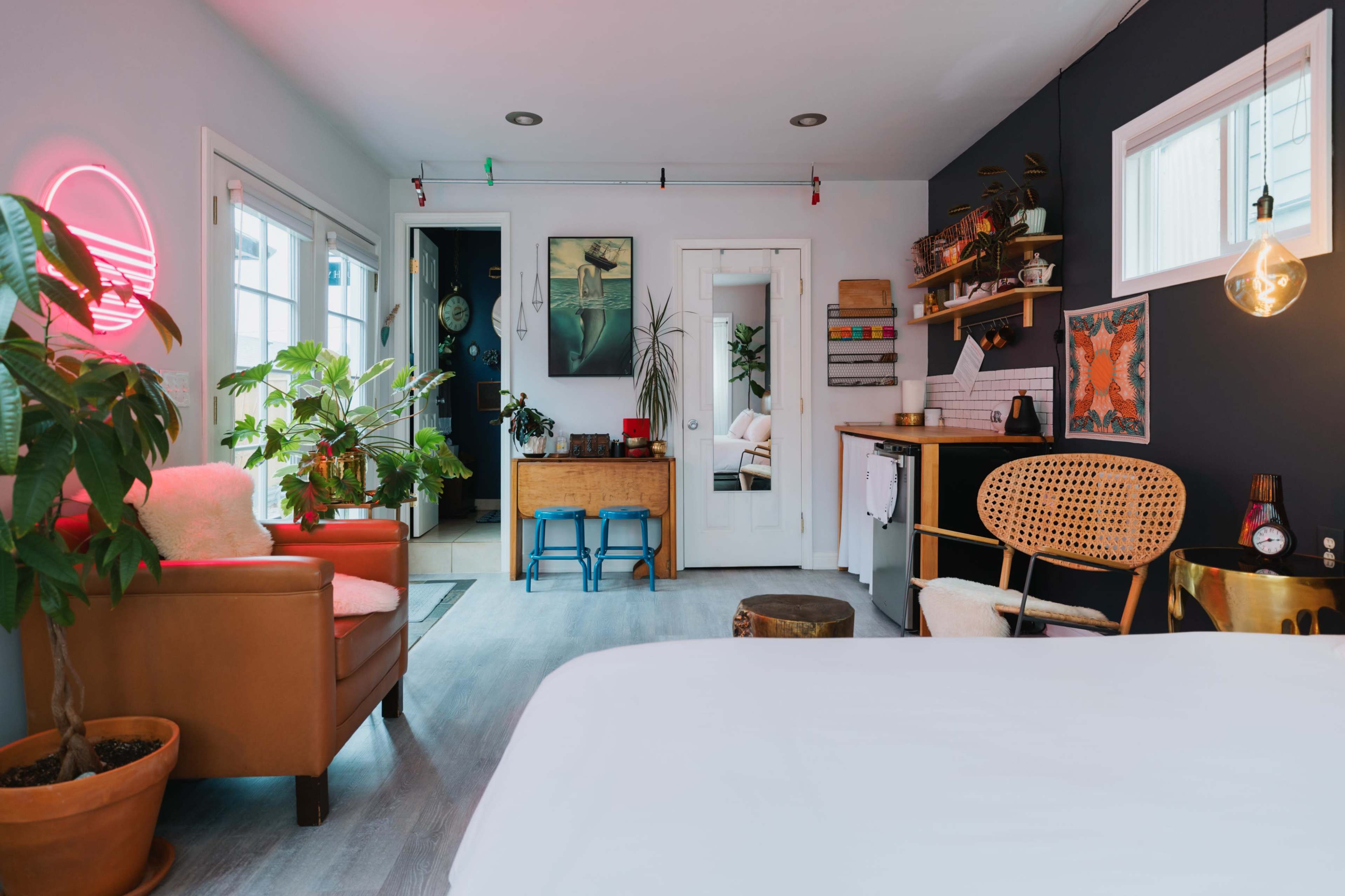 A cozy room features a mix of indoor plants, a vintage armchair, a wooden table, and decorative art on the walls.
