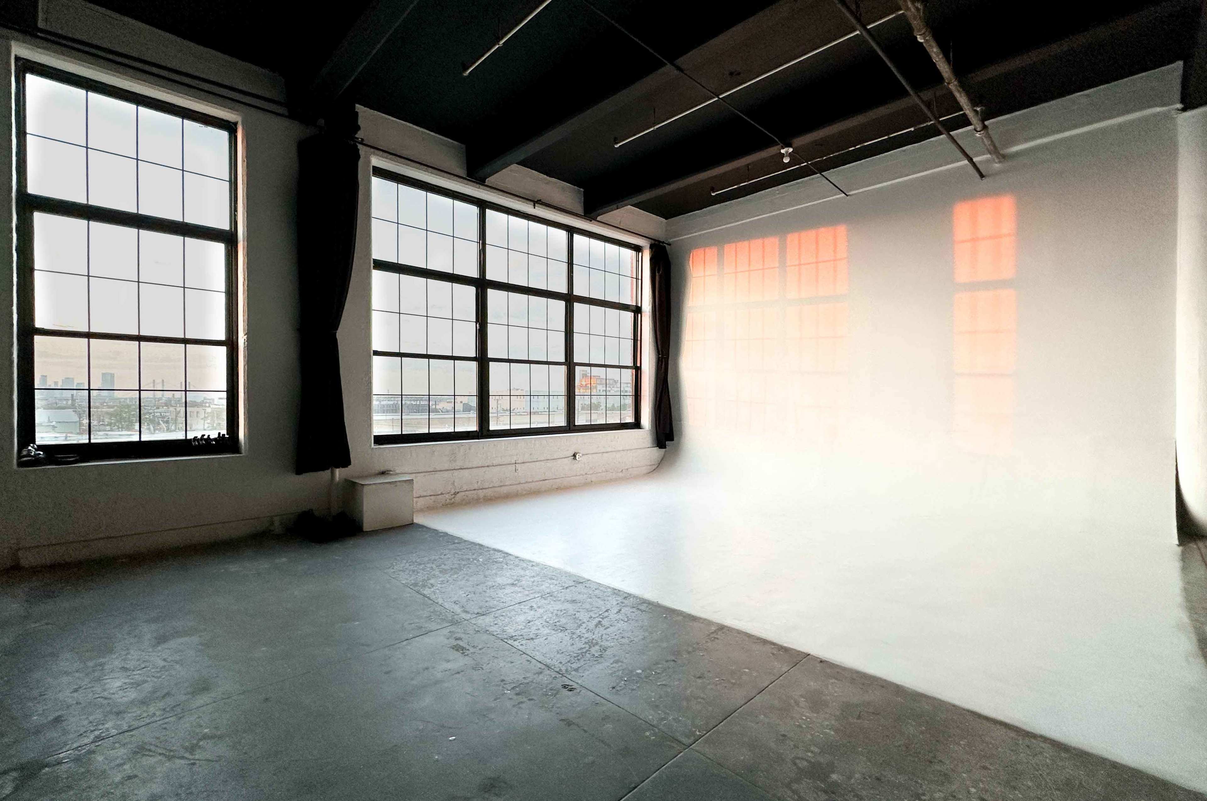 A spacious, well-lit interior room with large windows and a plain white wall.