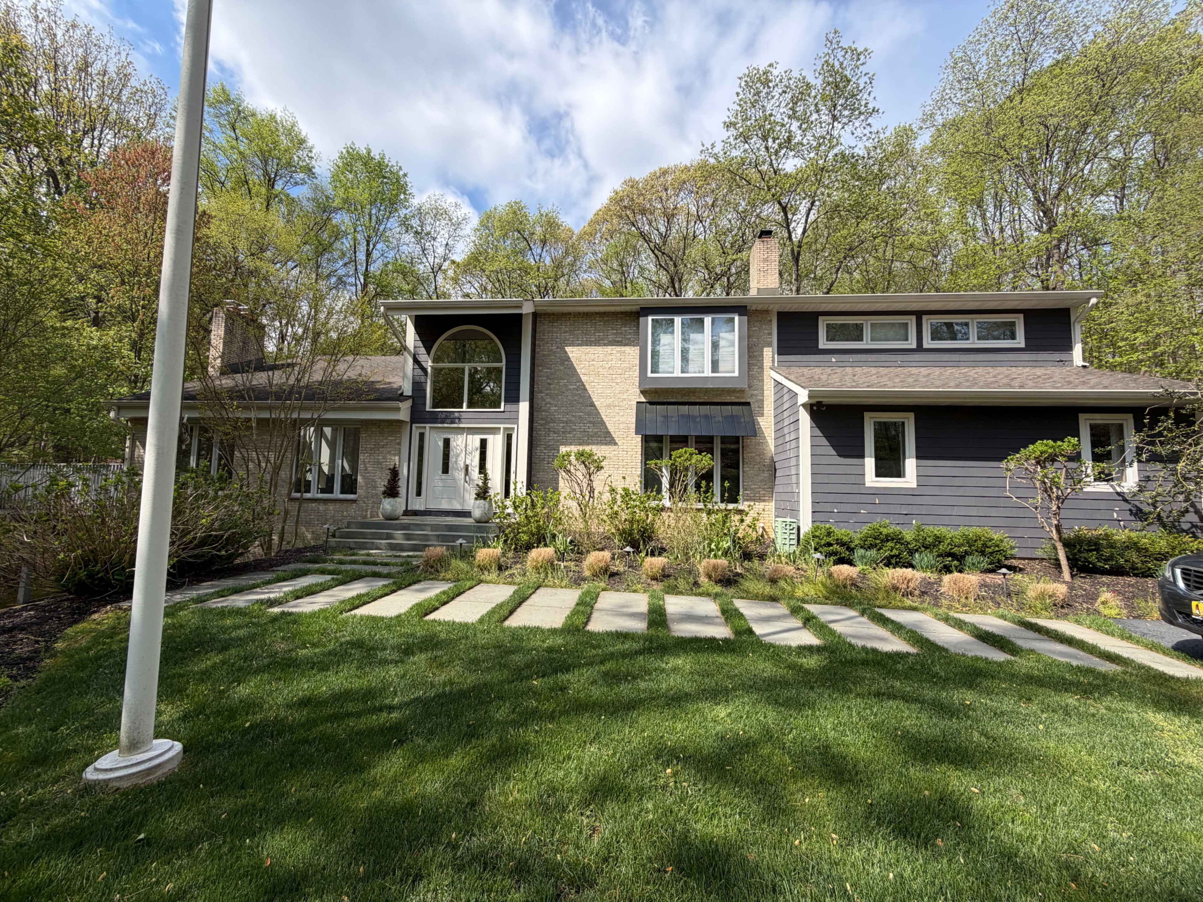The image shows a modern two-story house with a landscaped front yard featuring stone walkways and greenery.