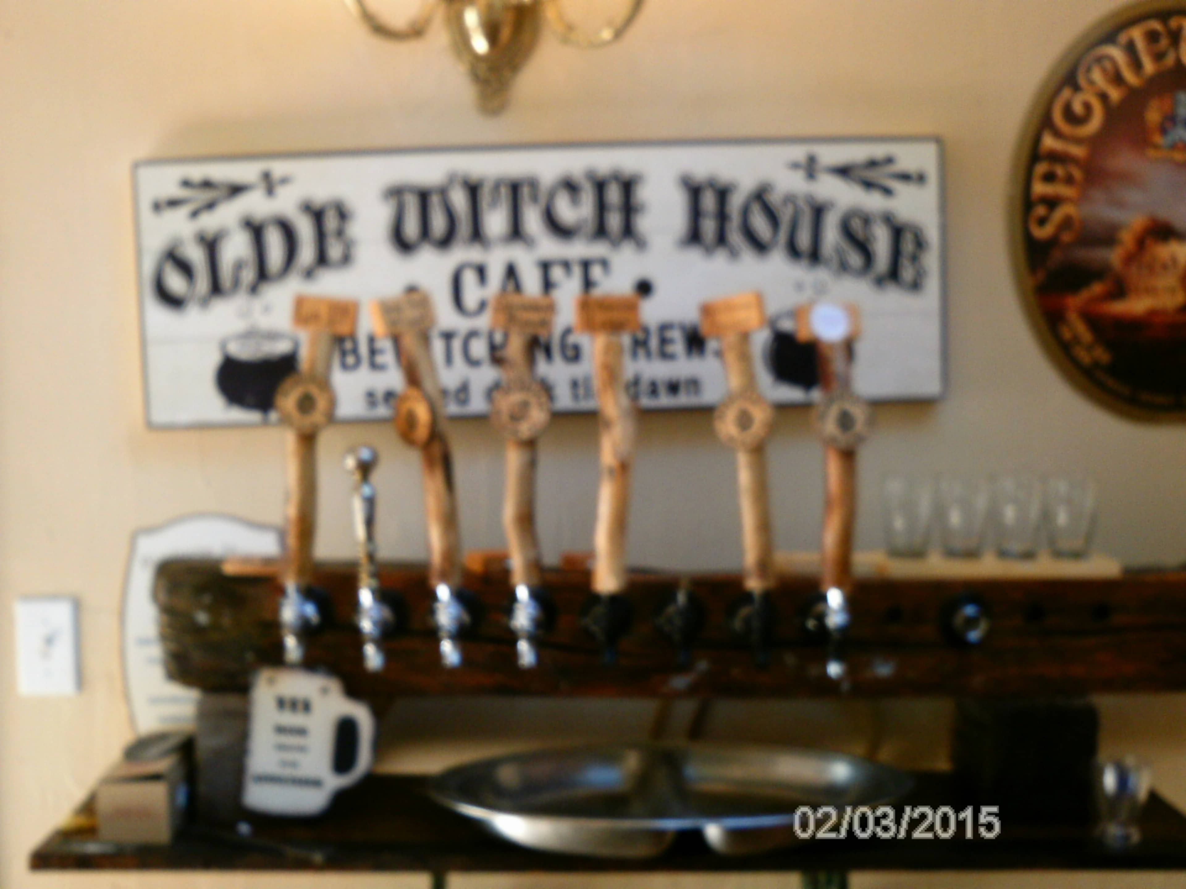 A wooden beer tap setup with multiple handles in front of a sign that reads "Olde Witch House Cafe."