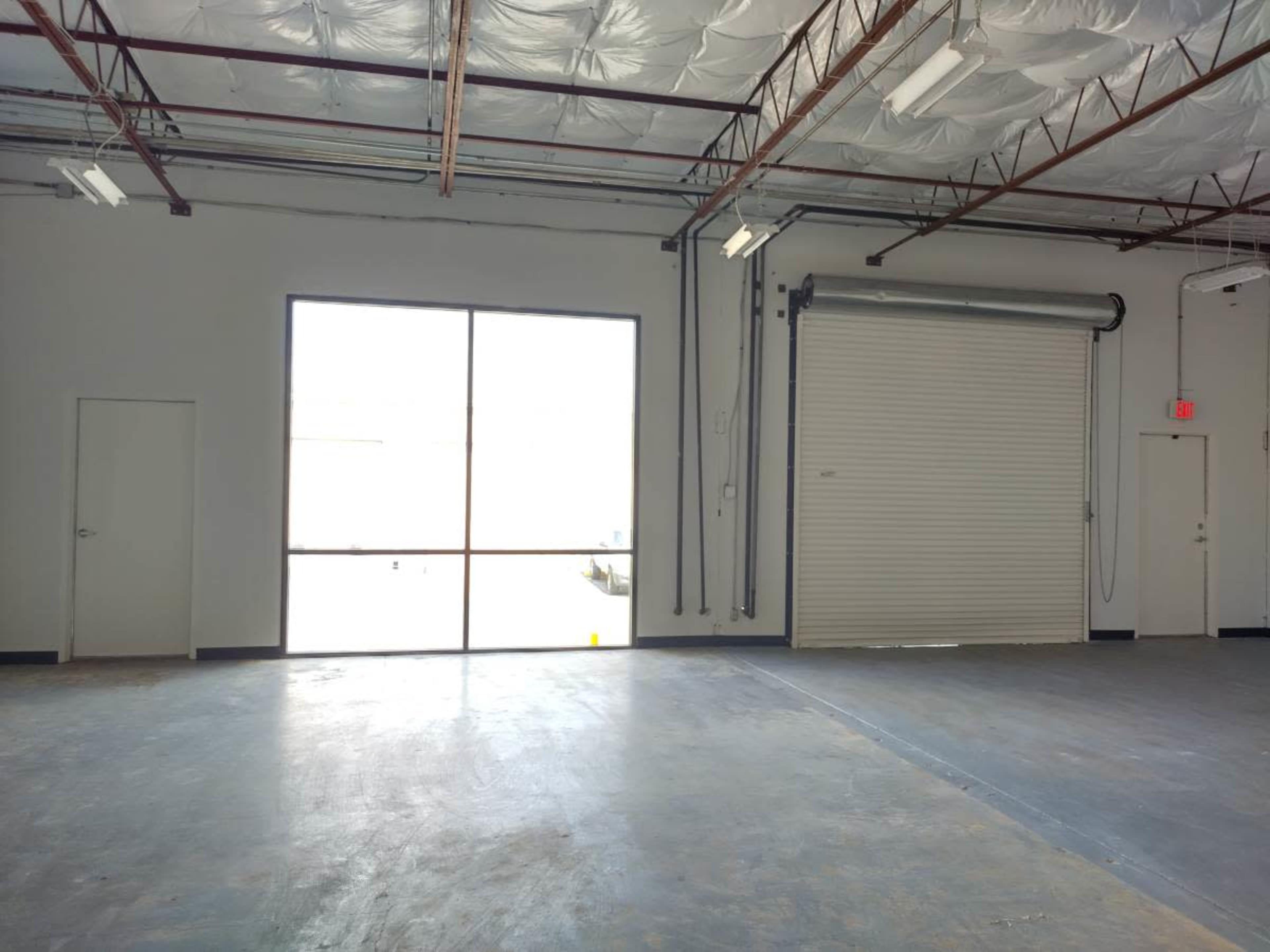 The image shows the interior of a spacious commercial warehouse with a large window and a roll-up door.