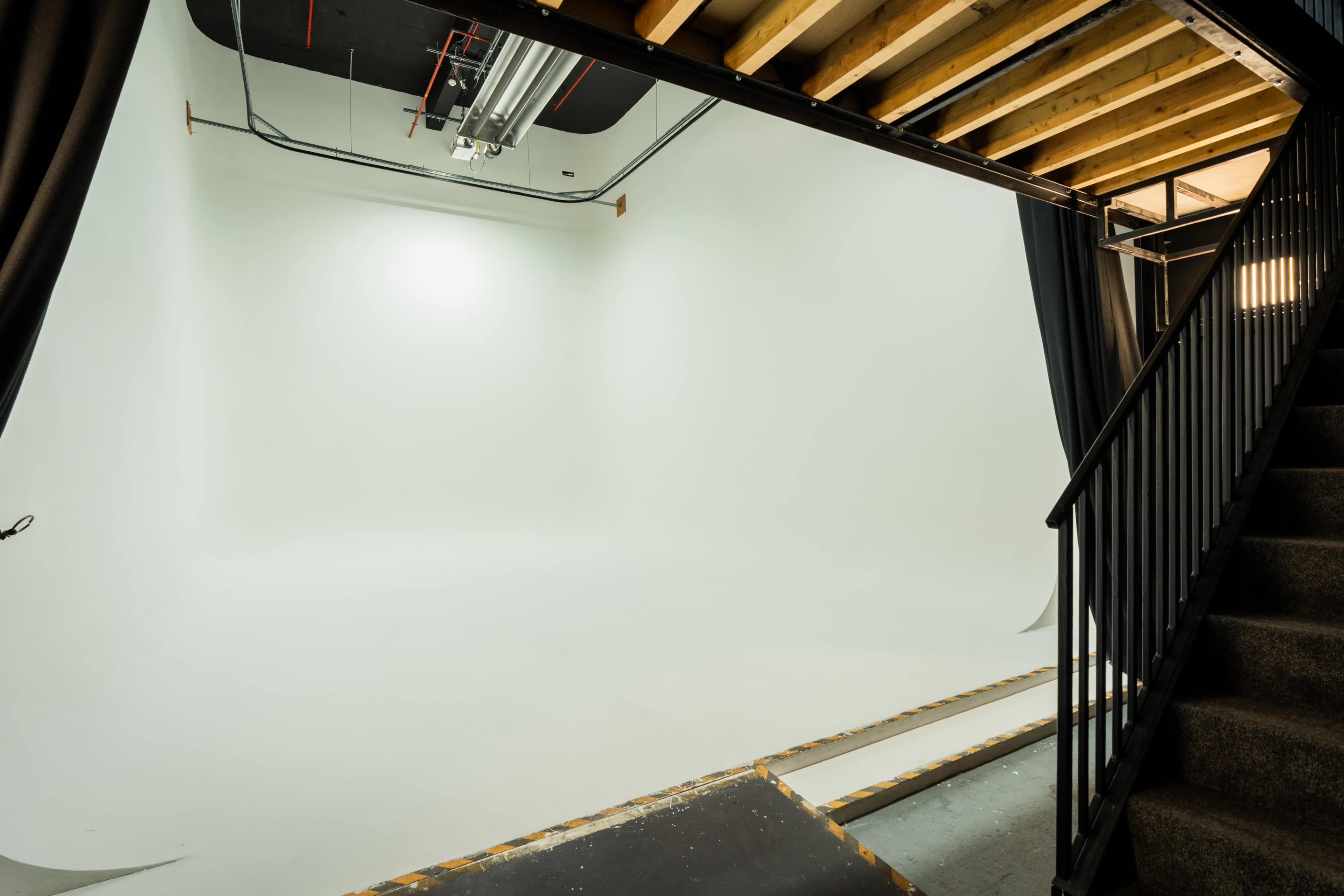 The image shows a staircase leading to a spacious, empty photo studio with white walls and a seamless backdrop.