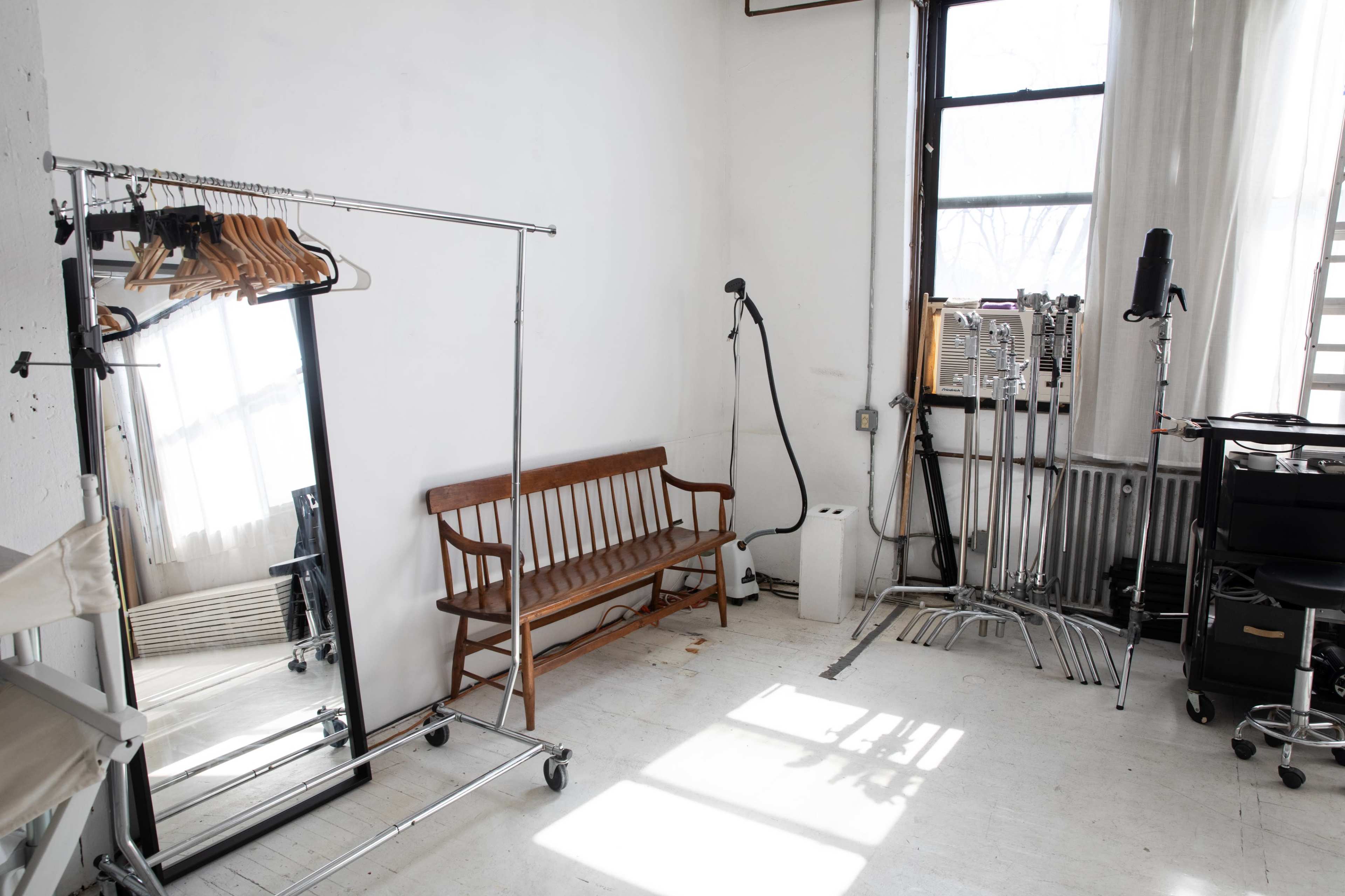 The room contains a wooden bench, a mirror on a clothing rack, and various stands and equipment against the walls.