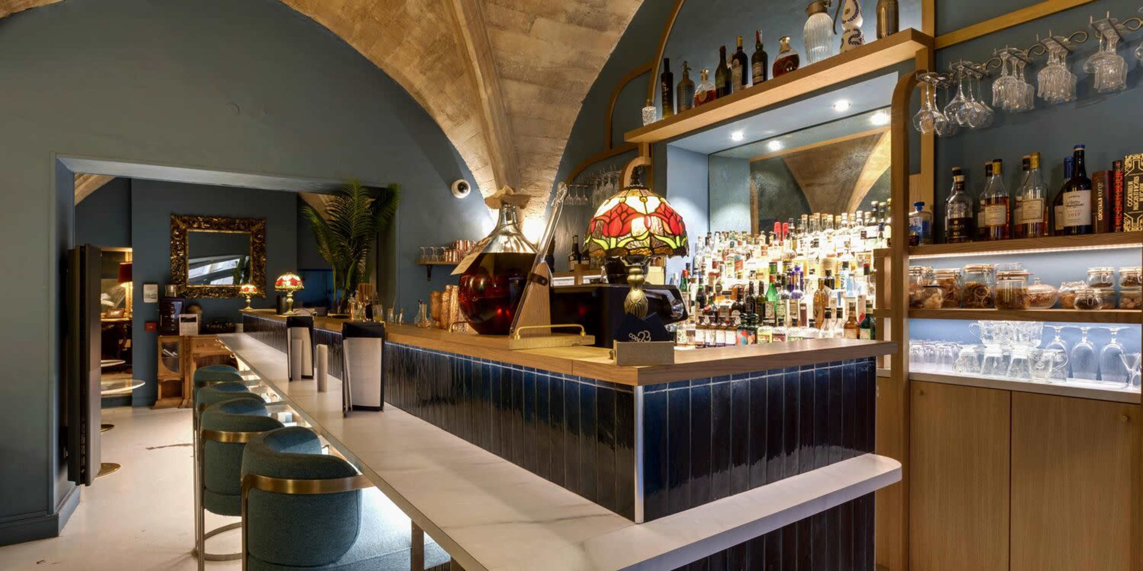 The image shows a bar area with a curved stone ceiling, a well-stocked back shelf of bottles, and a countertop with seating.