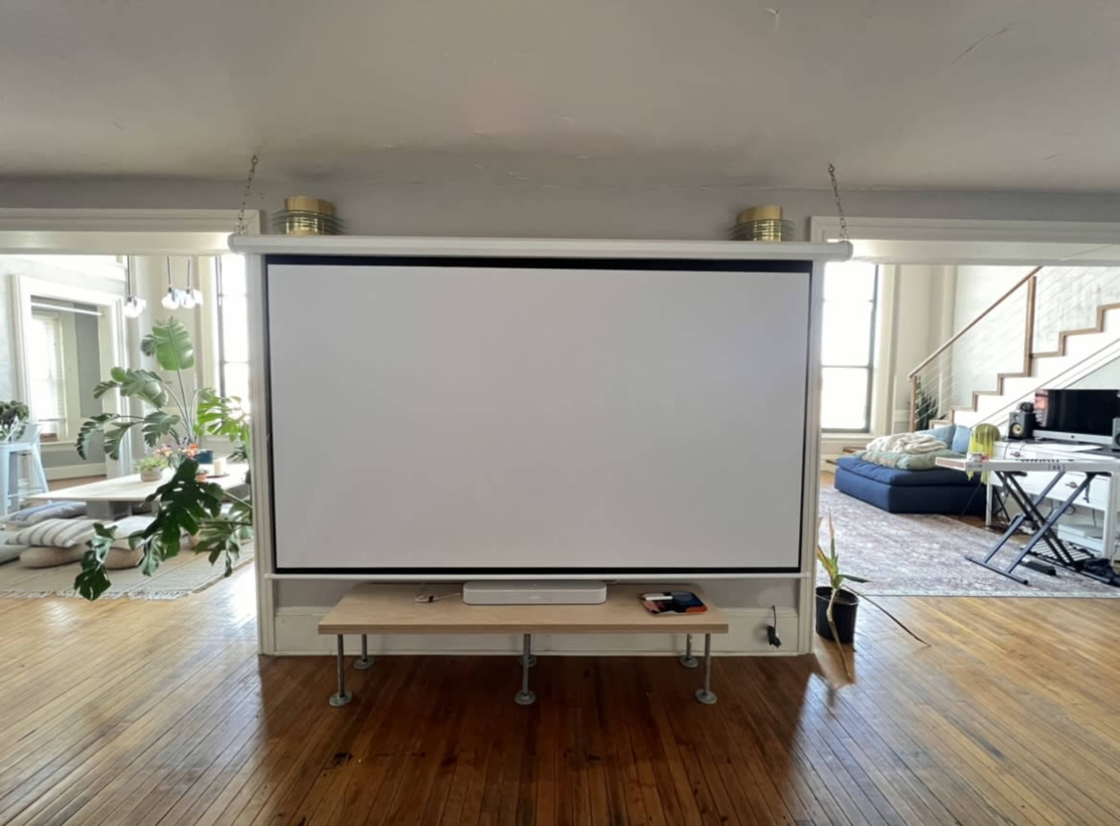 A blank projection screen is mounted on a wooden frame in a room with a minimalist interior and large windows.